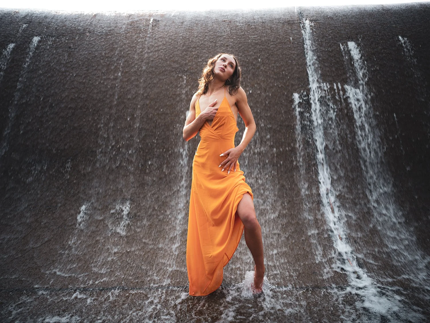 A woman in an orange dress standing in falling water