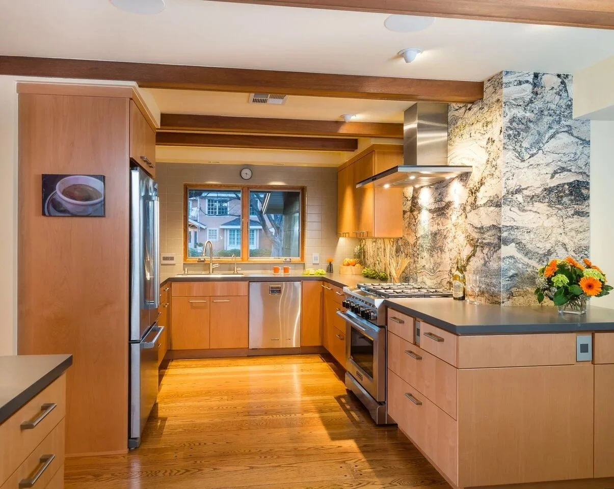 Light wood kitchen cabinets with exposed ceiling beams, a stone slab backsplash, and a window over the sink