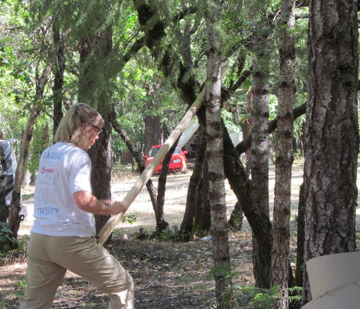 Sandee carved a walking stick for her second project. Here she is making used of two crossed tree trunks to hold her staff for rounding with the spoke shave.