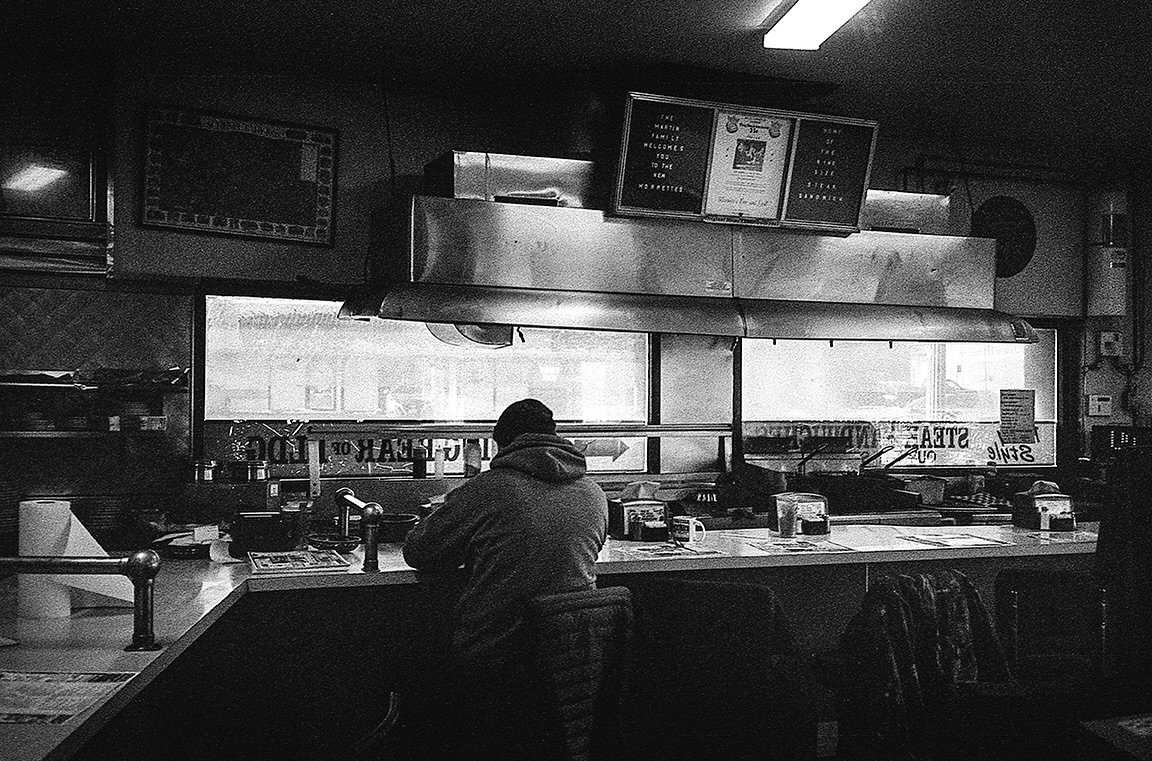 A single diner.
One spoon. One fork. One knife.
Stale silence in thick, greasy air.
&ldquo;What&rsquo;ll it be?&rdquo;
The special&mdash;hold the slaw.
A blank stare,
a nod,
a muttered please and thank you.
The squeak of a vinyl stool,
shaped by hund