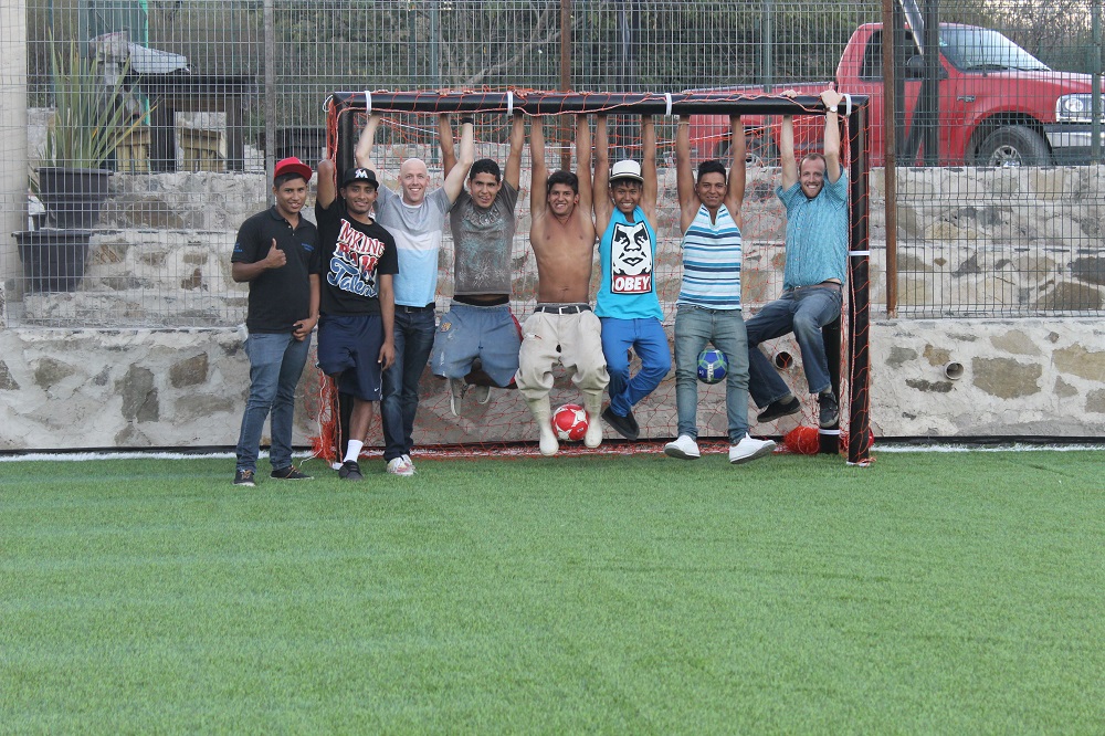 The soccer field is made of synthetic grass with a small rock and steel fence perimeter. 