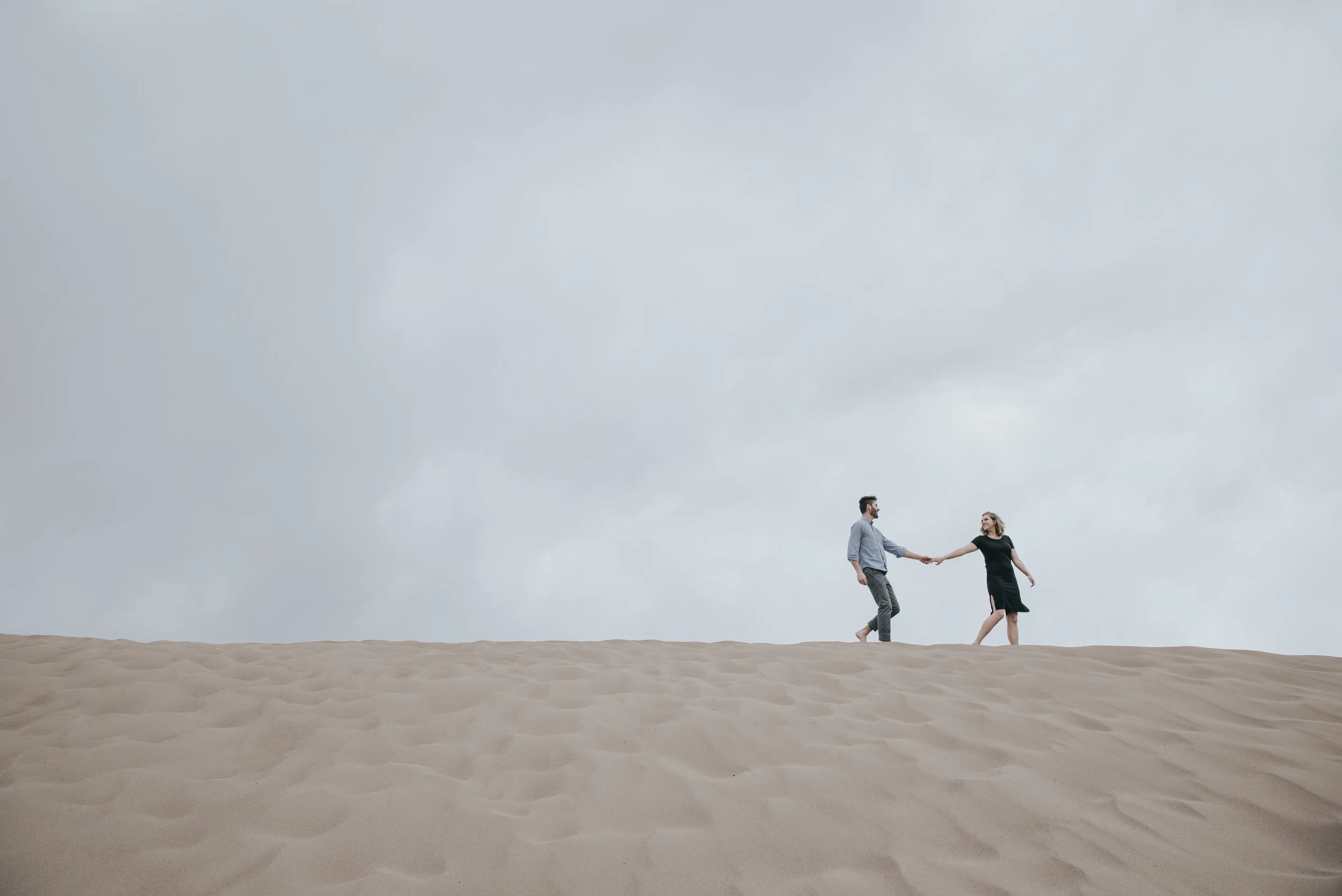 A couple walks along a sand dune holding hands having chosen a location for their elopement or wedding