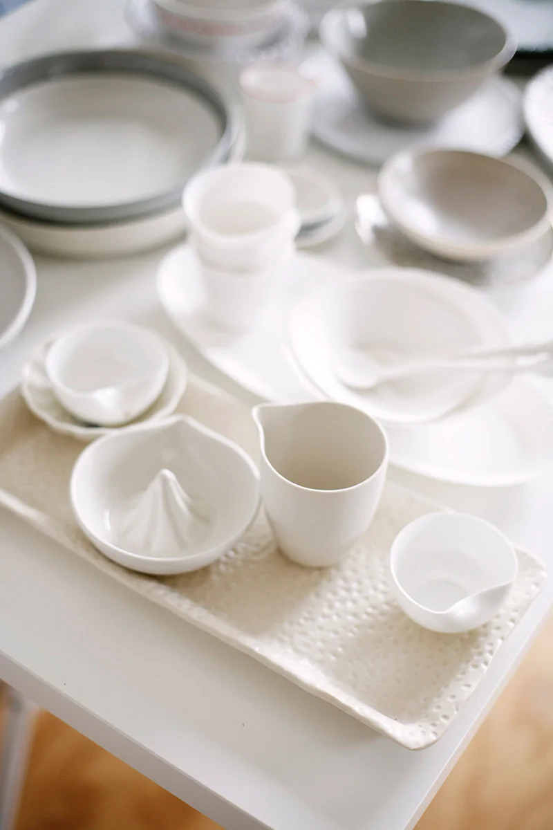 A collection of white porcelain dishes, bowls, and cups arranged on a textured tray, with some dishes stacked and others placed separately.