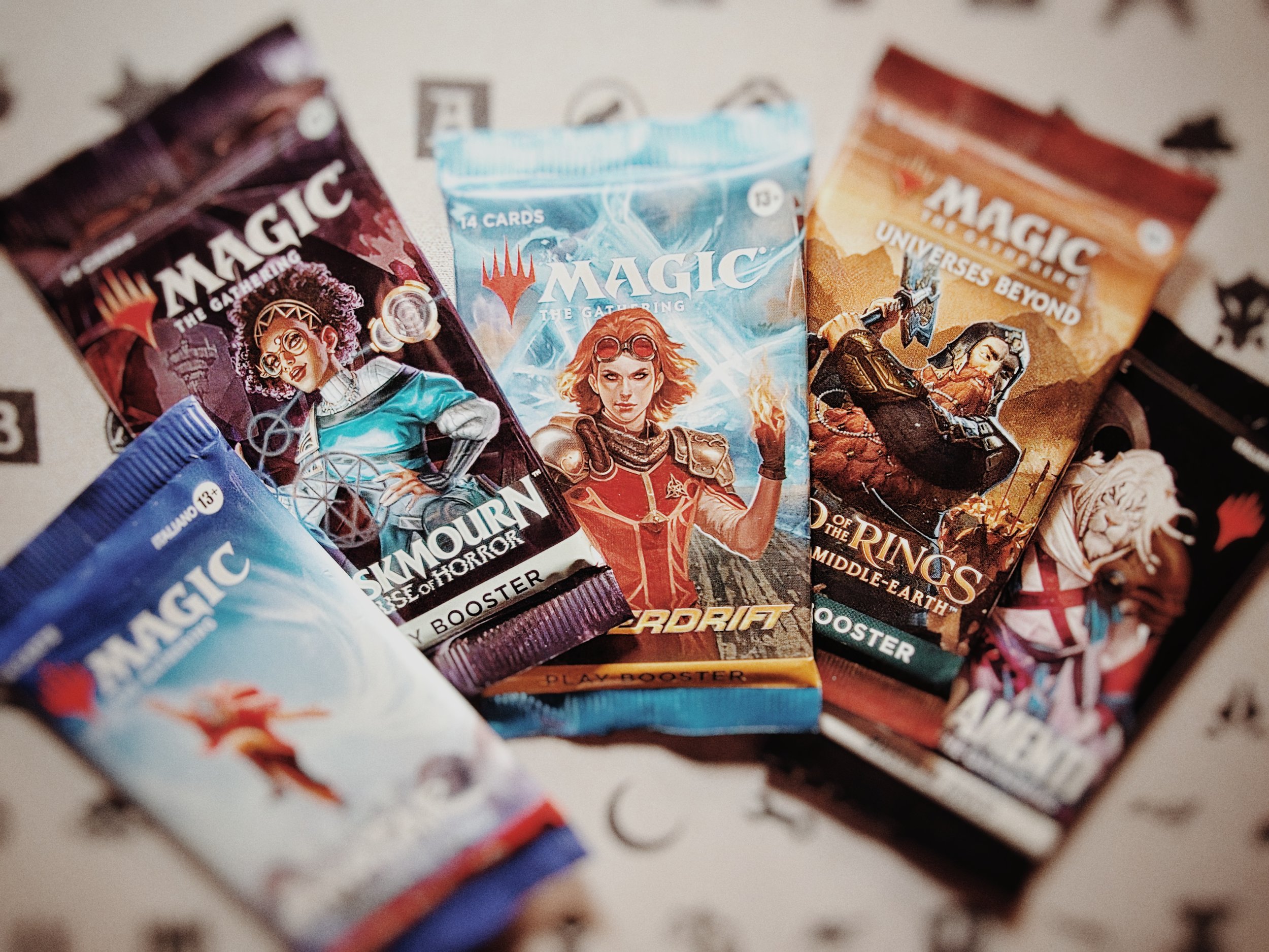 Pacchetti di carte da gioco di Magic The Gathering con vari personaggi fantasy su ogni confezione, disposti su una superficie con disegni.