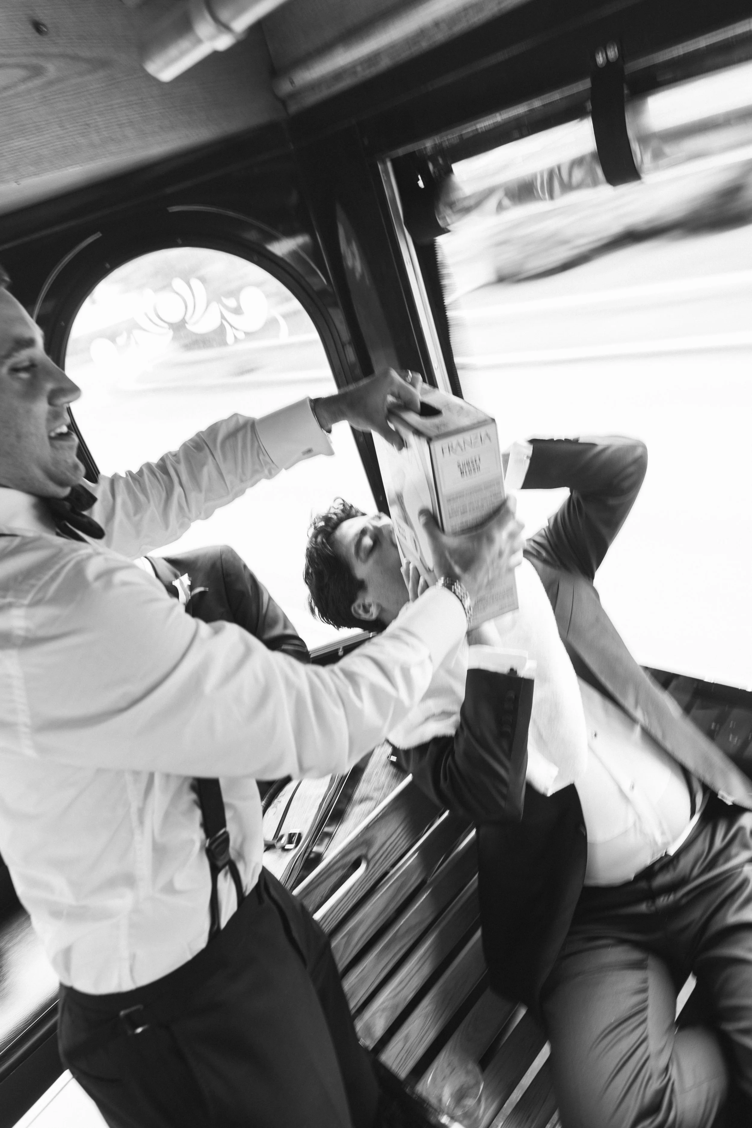 Three men in formal attire inside a bus, with one man handing a box to another.