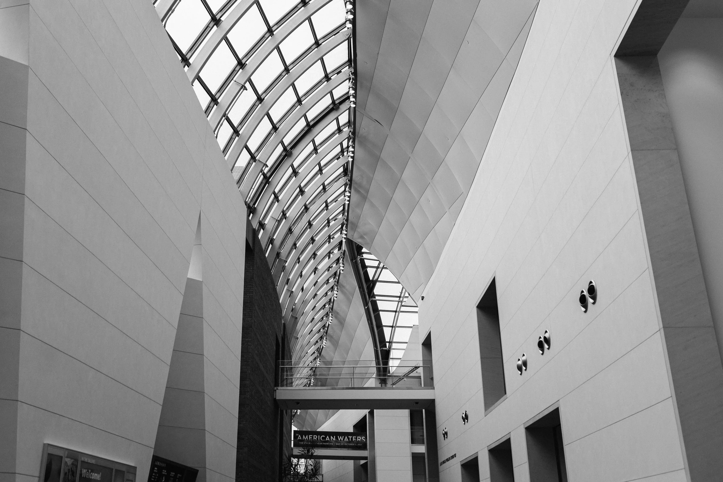 Interior view of a modern building with curved glass ceiling, white walls, and multiple floors visible through open spaces.