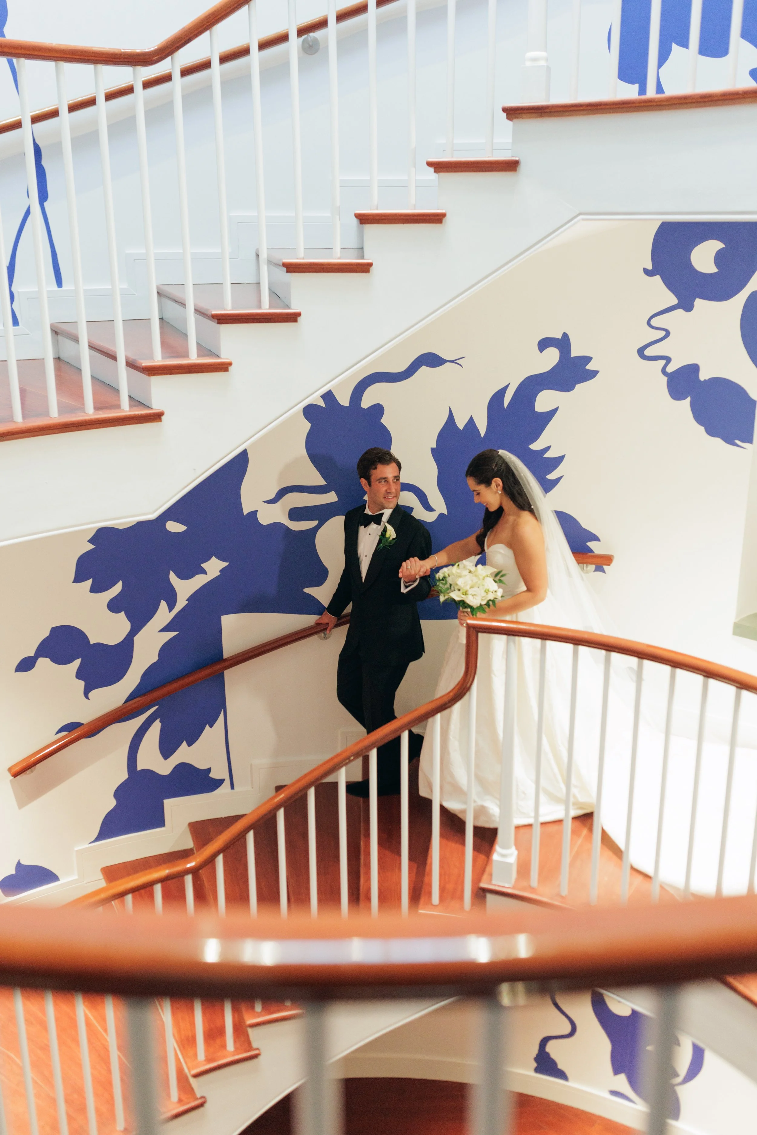 A bride and groom holding hands on a staircase with blue lion artwork on the wall.