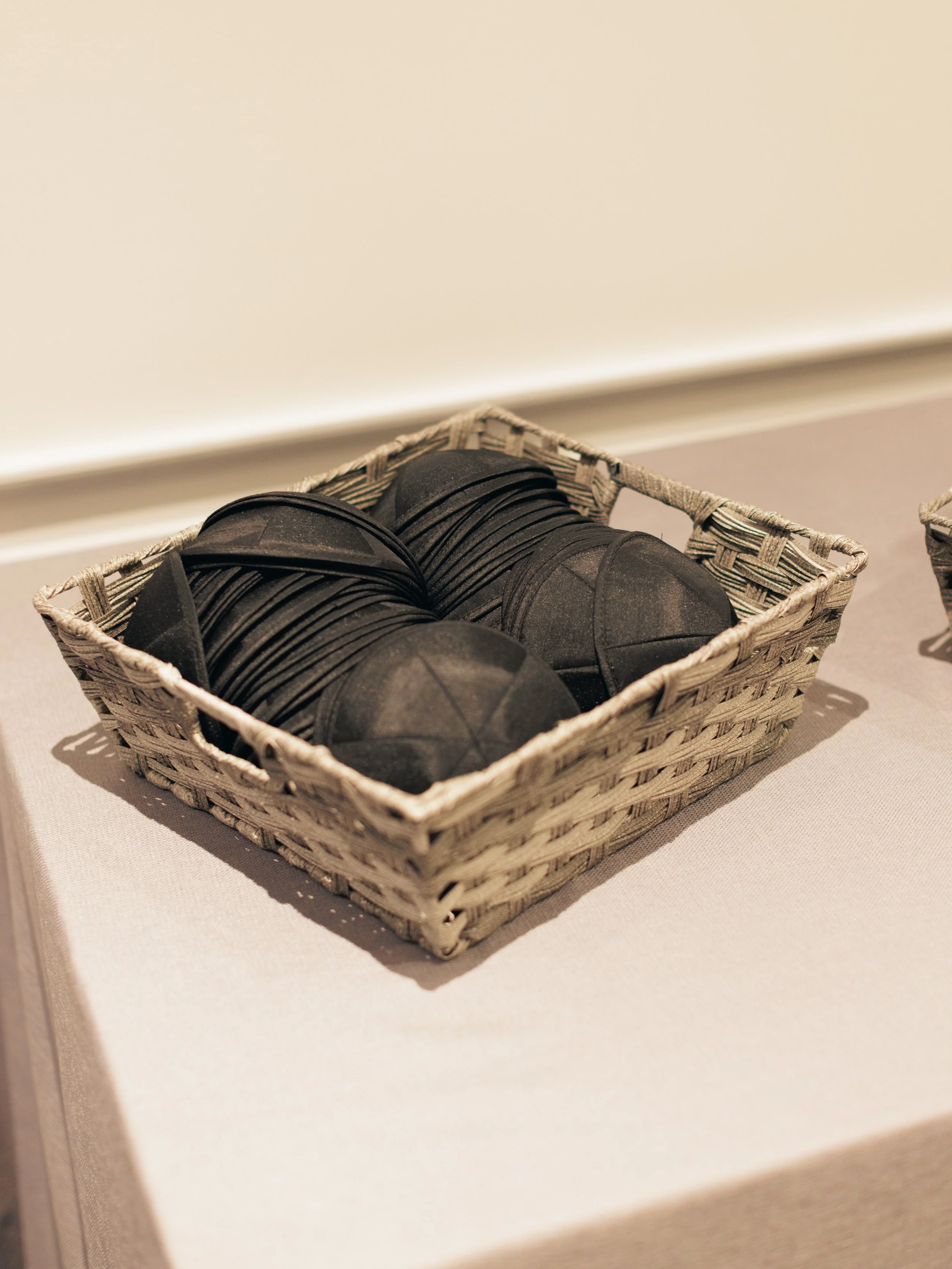 A woven basket filled with black flat slippers placed on a white table.