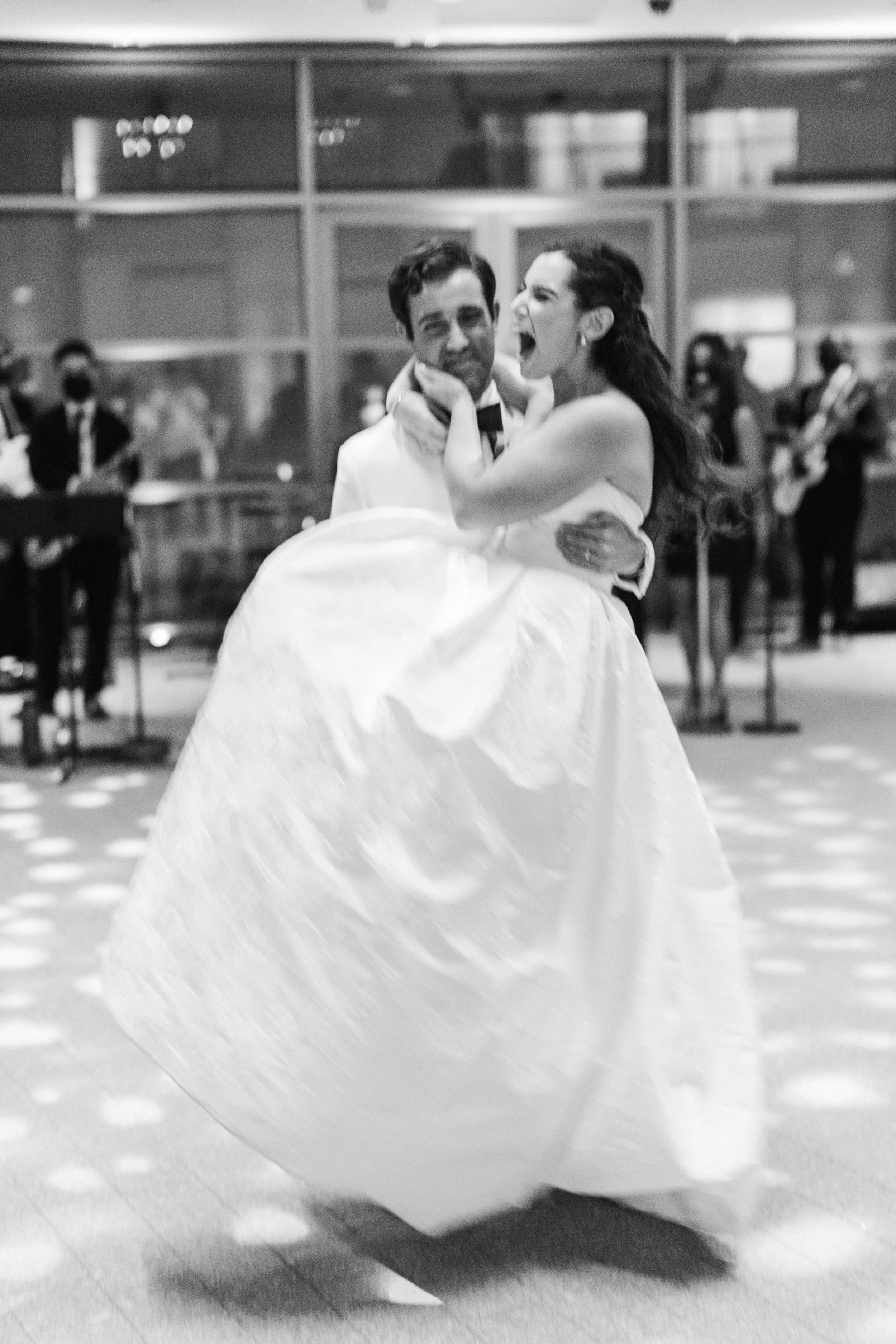 A ballroom dance couple performing a waltz, with the woman in a white gown and the man in a tuxedo, surrounded by a band playing in the background.