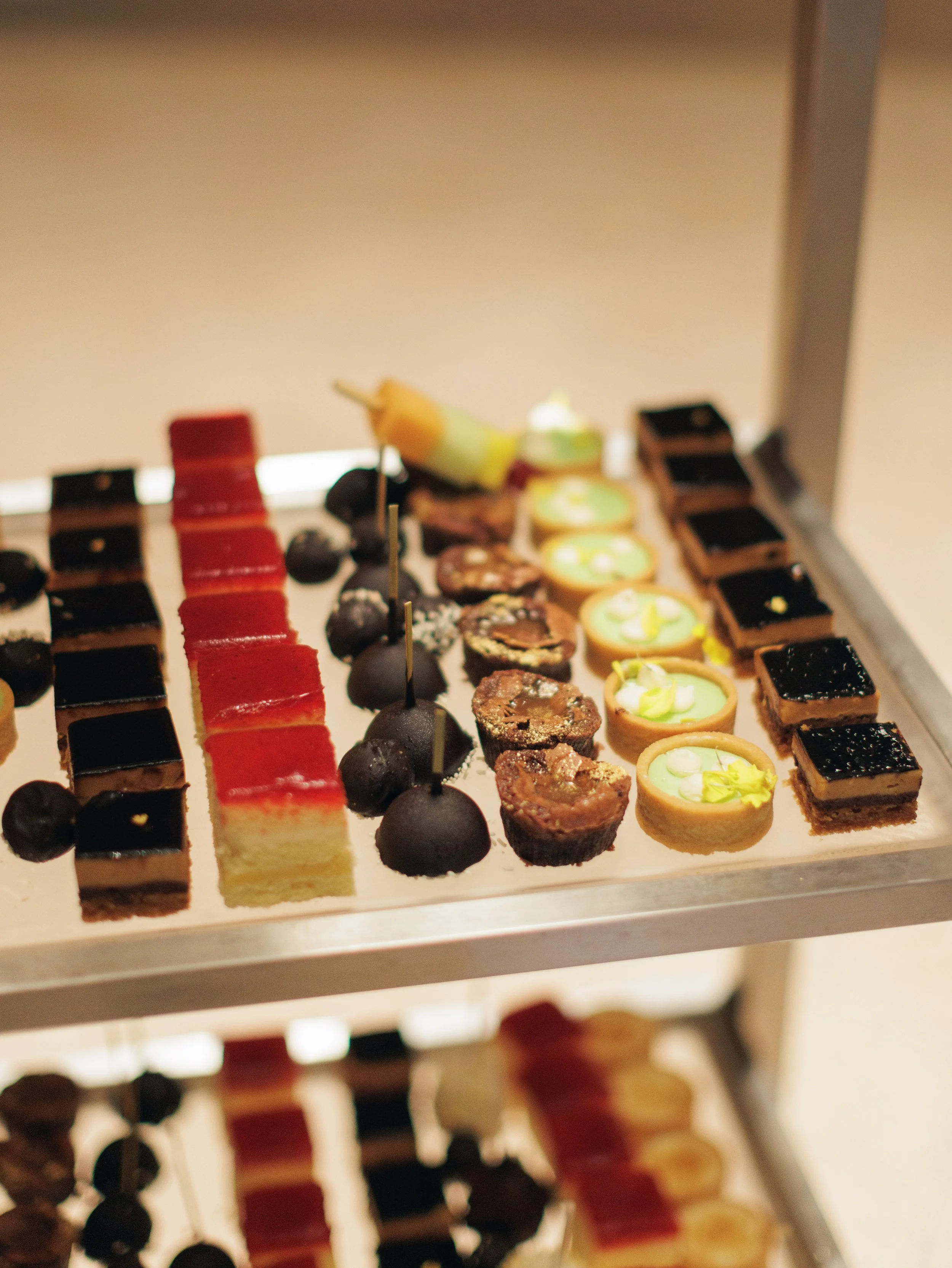 A tray of assorted mini desserts including tartlets, chocolates, and layered cake squares.