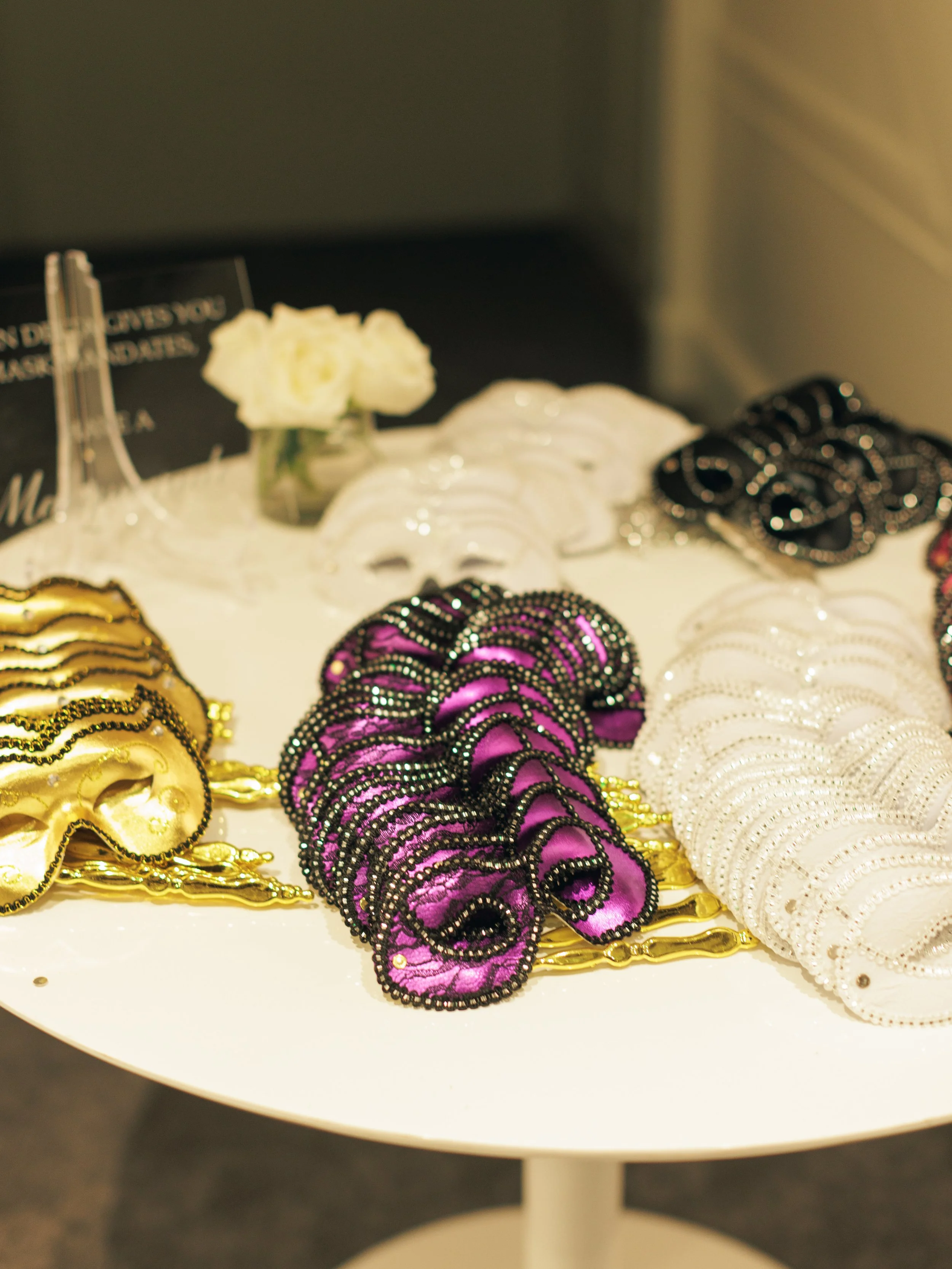 Display of decorative headbands in gold, purple, and white colors, arranged on a white table with flowers and a black sign in the background.