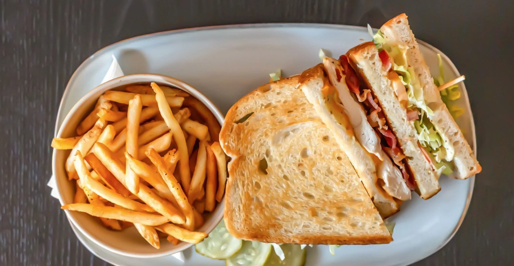 Partial sandwich with lettuce, tomato, turkey, and cheese on toasted bread, served with a side of French fries in a bowl.