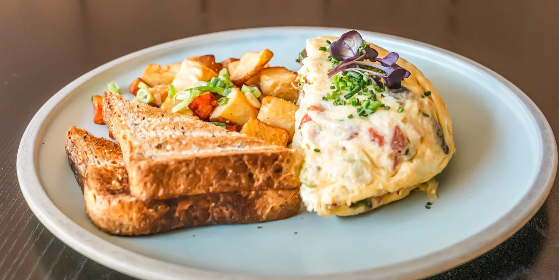 Plate with toasted bread, roasted potatoes, and a creamy vegetable and meat casserole garnished with chopped chives and microgreens.