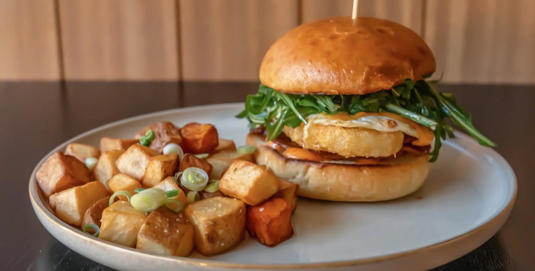 A plate with a gourmet sandwich and roasted potatoes, garnished with sliced green onions.