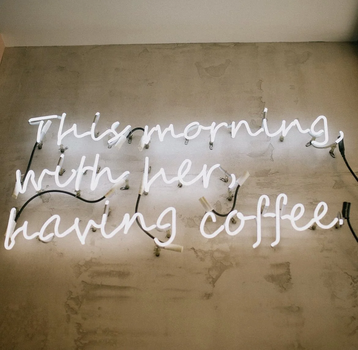 Neon sign with the quote by Johnny Cash: 'Thursday morning, with her having coffee,' mounted on a plain wall.