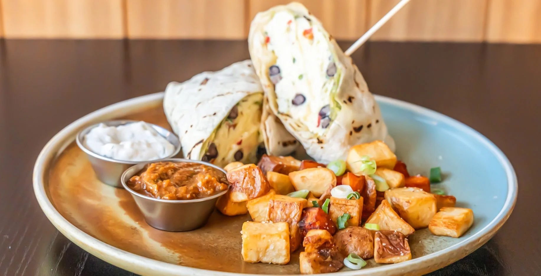 Plate of stuffed tortillas with sides of roasted potatoes, sour cream, and salsa