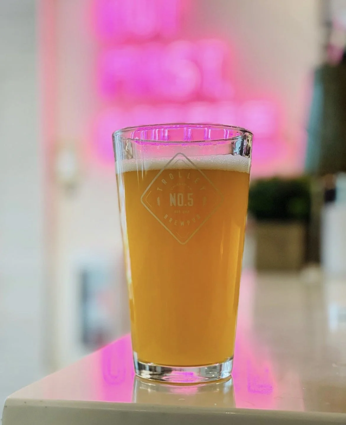 A glass of beer on a table with pink, blurry posters in the background.