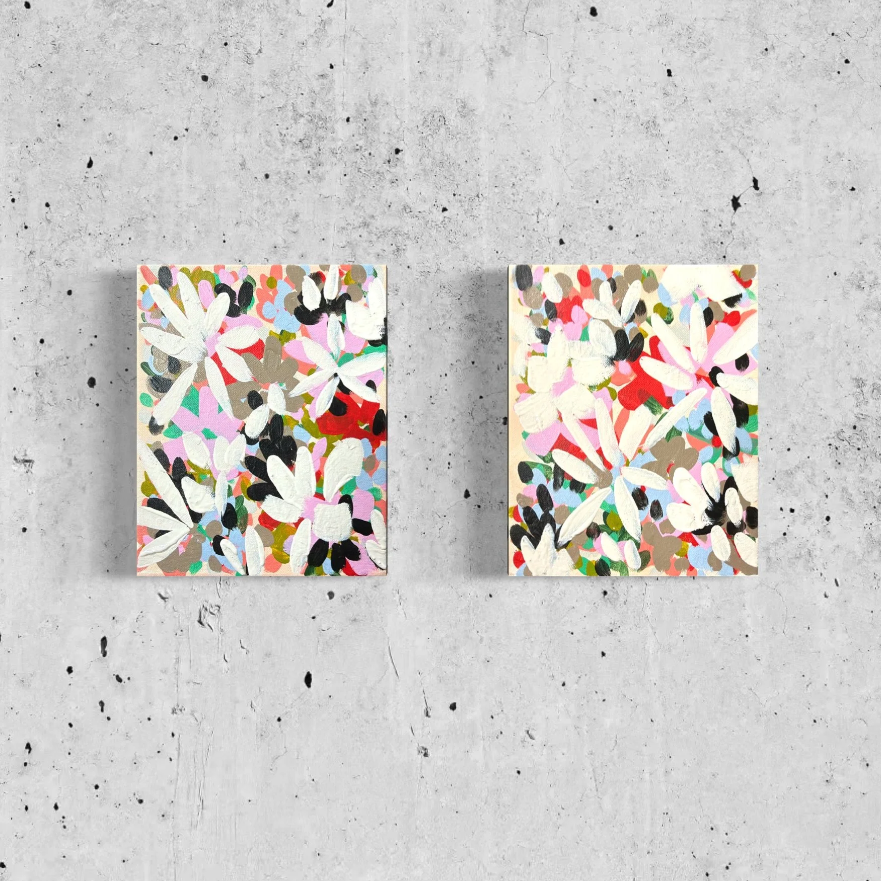 Two abstract floral paintings with white, pink, black, brown, and green colors hung on a gray concrete wall.