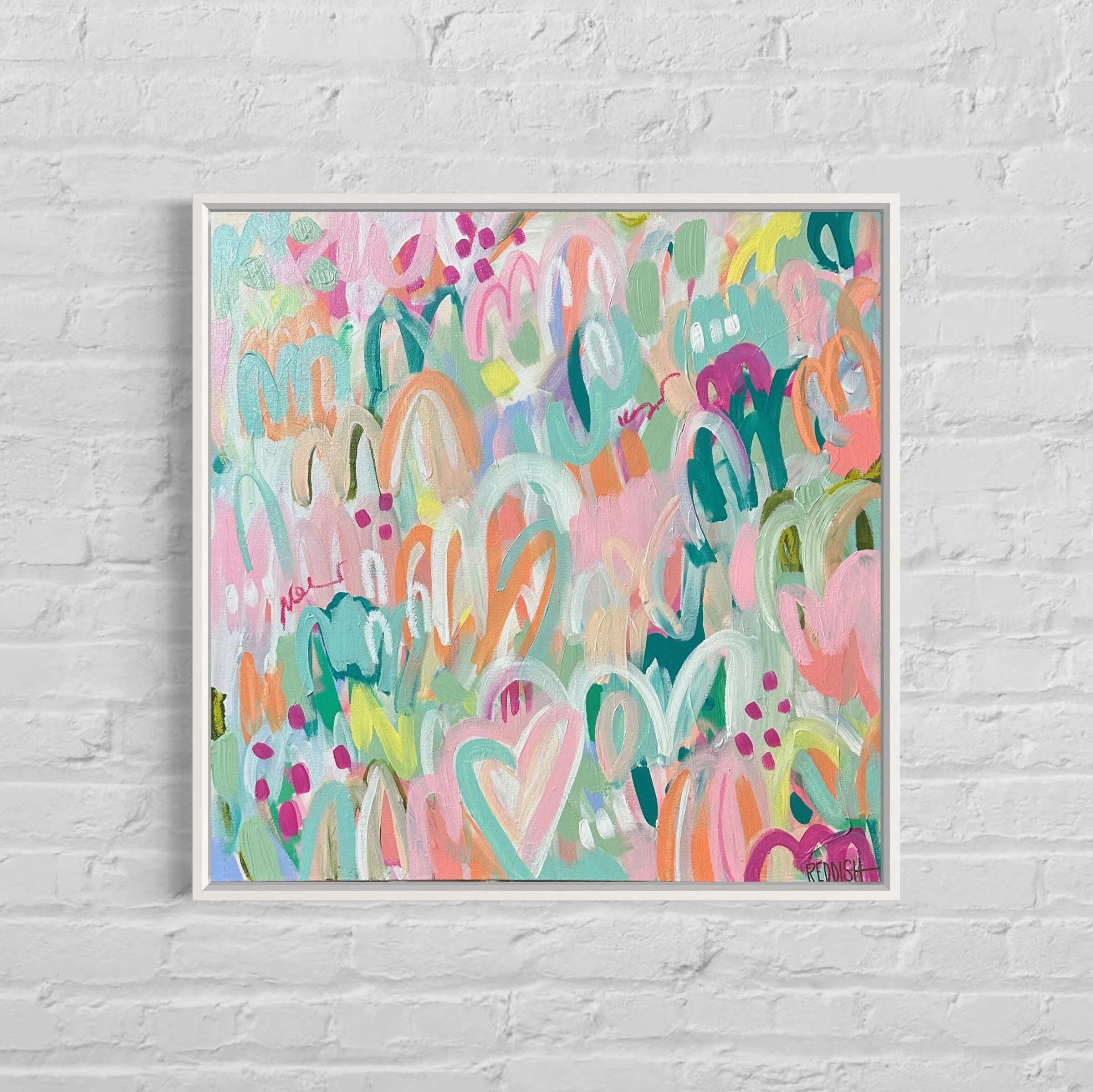 A colorful abstract painting with pastel and vibrant shades, featuring swirling shapes and patterns, framed and mounted on a white brick wall.
