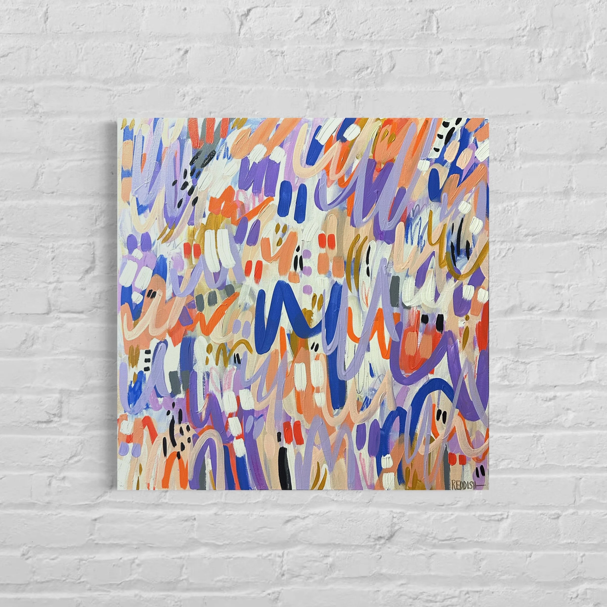 Abstract colorful painting with brushstrokes of orange, purple, blue, white, black, and gold, signed 'REDDISH' in the bottom right corner, hung on a white brick wall.