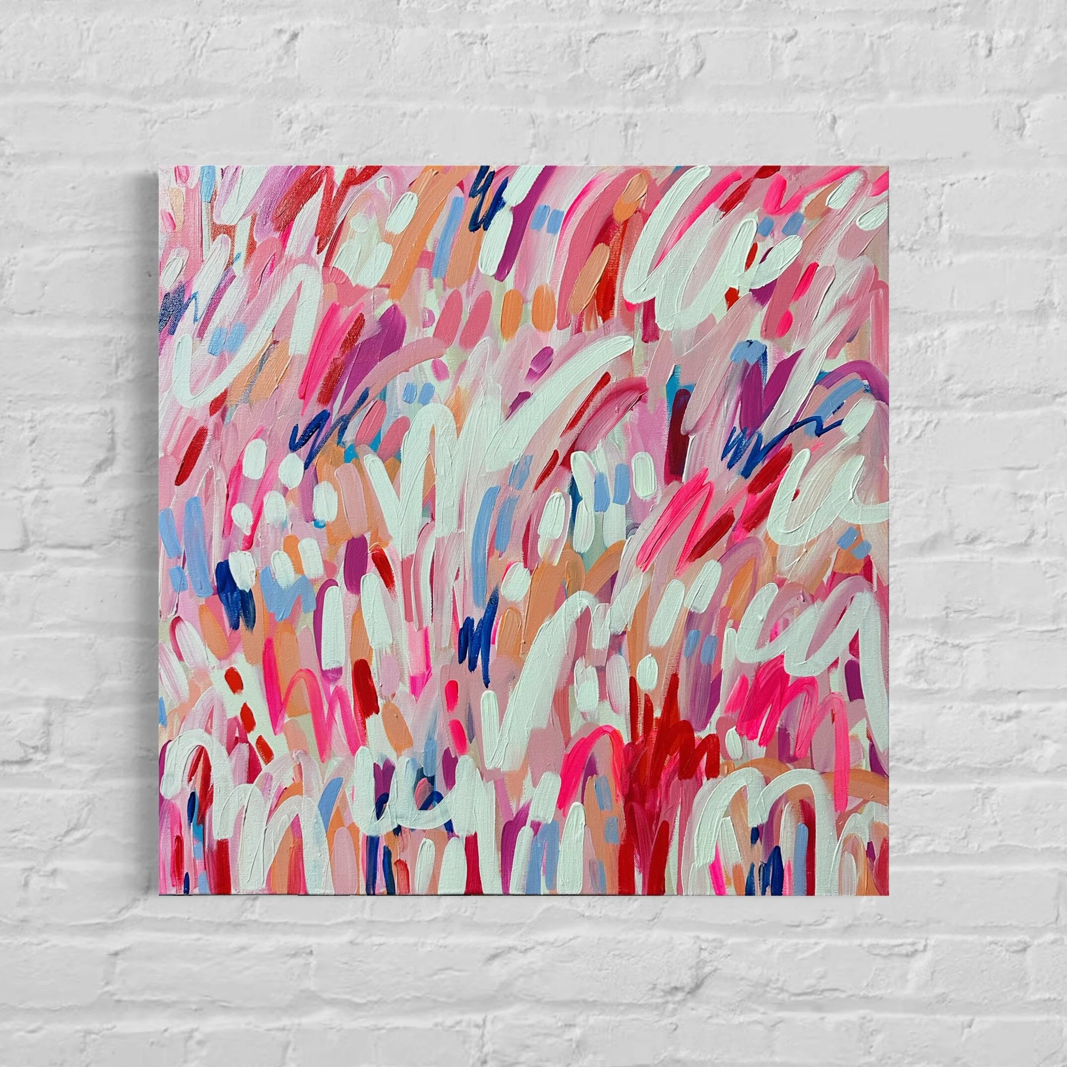 Close-up of an abstract colorful painting with brushstrokes of pink, red, white, blue, orange, and purple hues, mounted on a white brick wall.