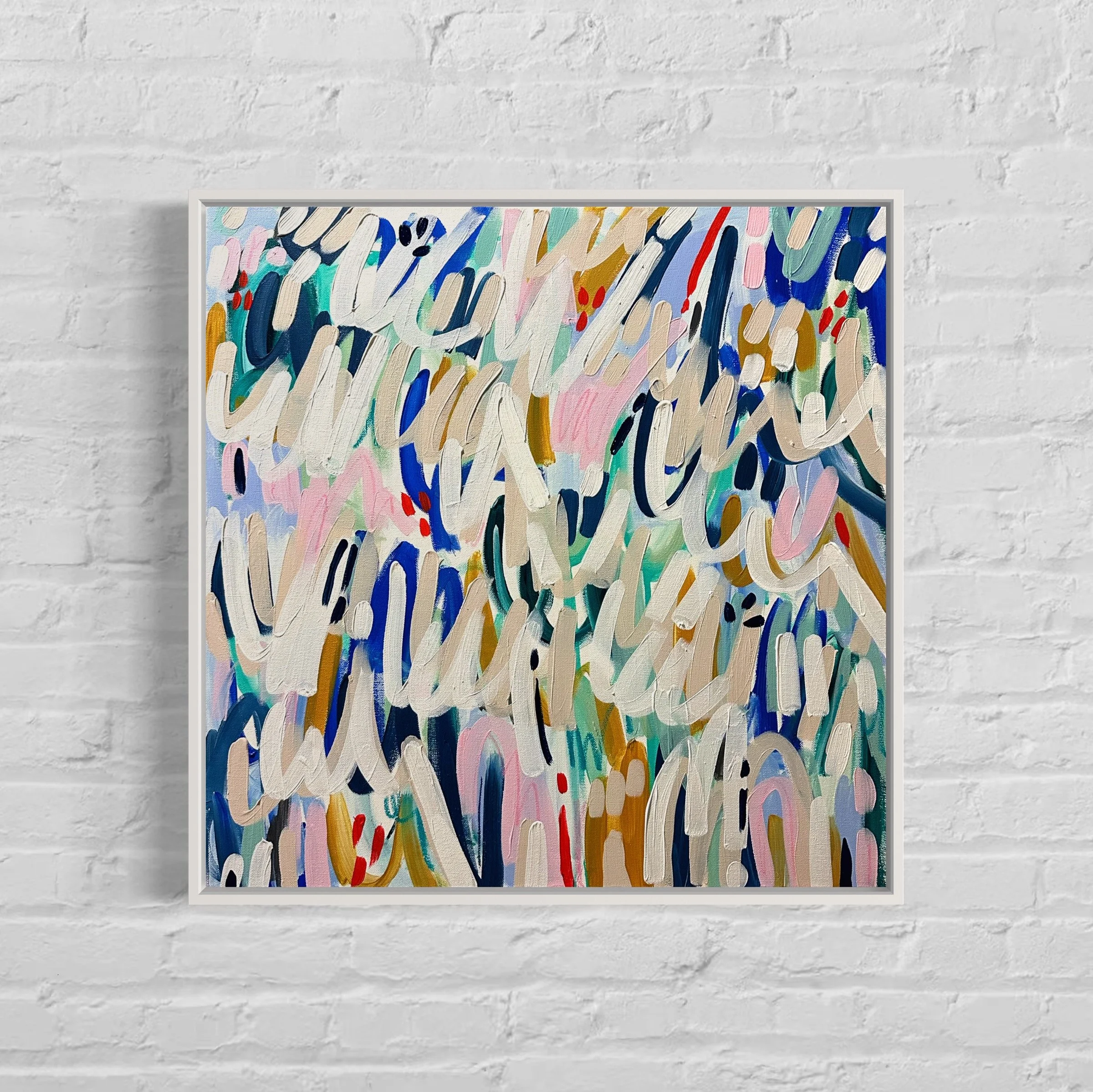 Abstract colorful painting with brushstrokes in blues, pinks, browns, and blacks, framed and hanging on a white brick wall.