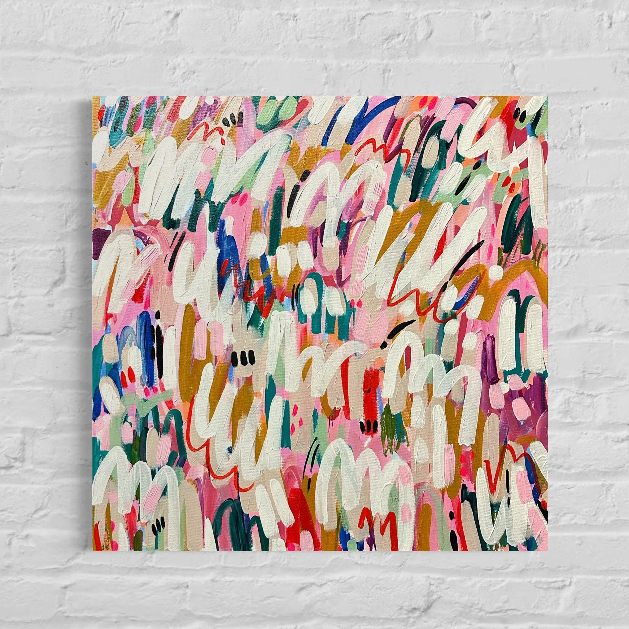 A colorful abstract expressionist painting with bold brushstrokes in pink, white, red, blue, green, and gold, displayed against a white brick wall.