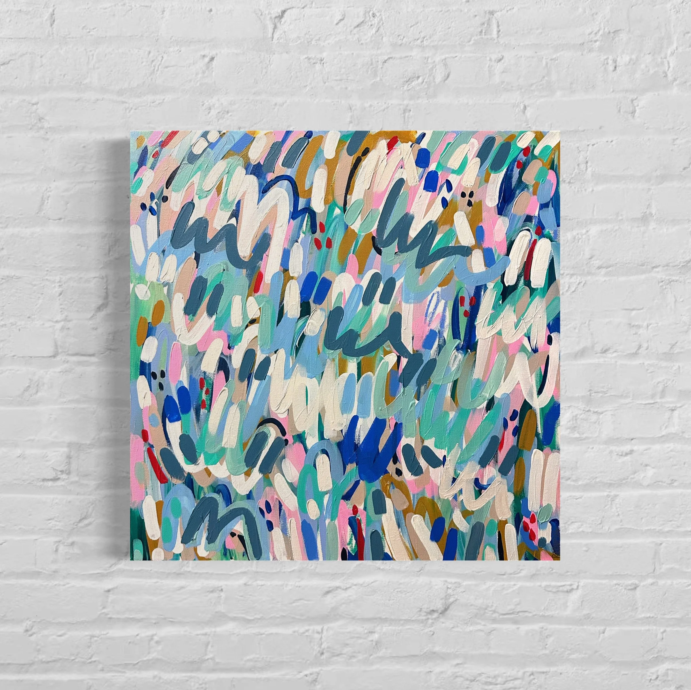 An abstract colorful painting with various brushstrokes and colors including pink, blue, green, tan, red, black, and white on a canvas, mounted on a white brick wall.