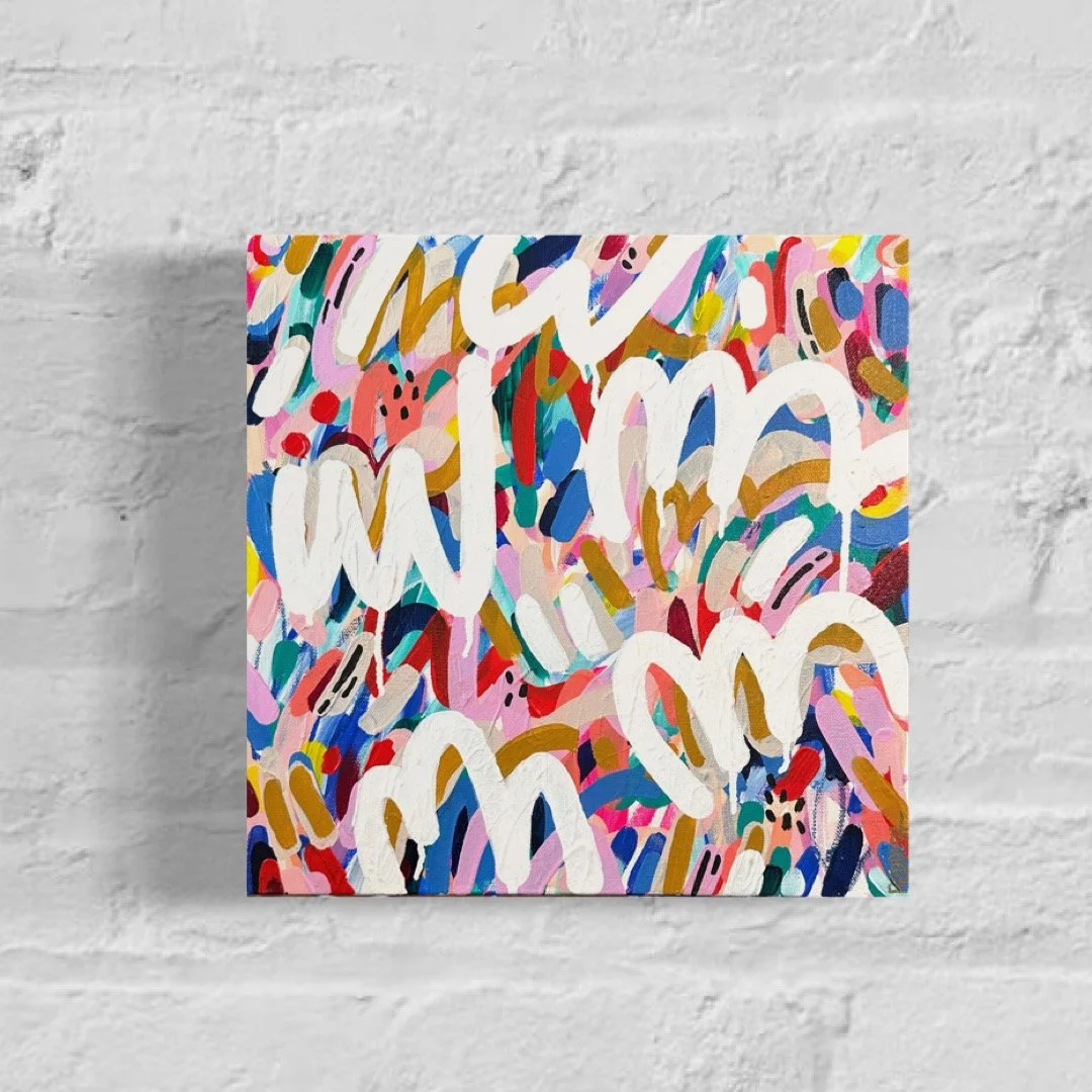 Colorful abstract painting with various shapes and bold white lines on a canvas, mounted on a white brick wall.