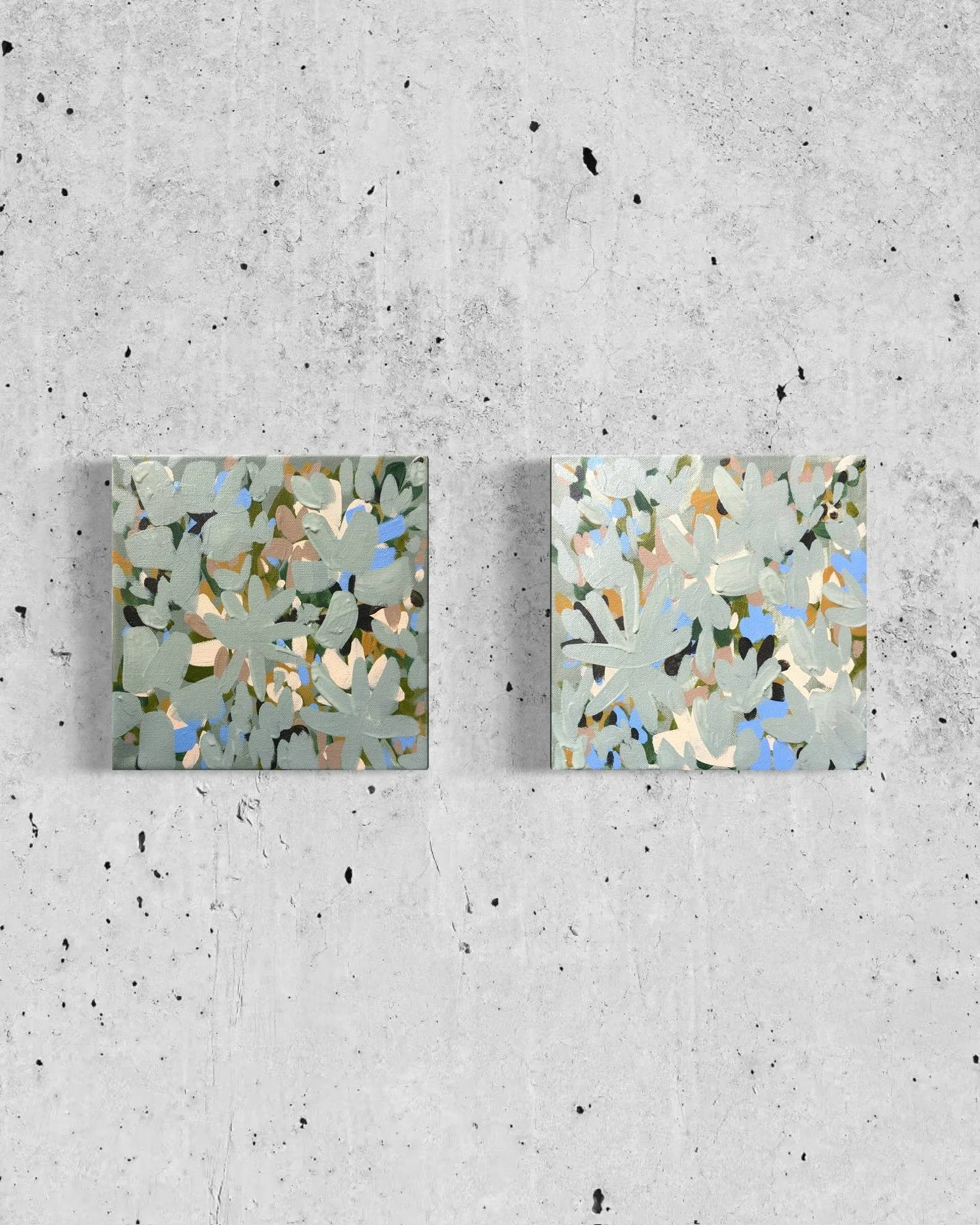 Two abstract floral paintings hung on a concrete wall.