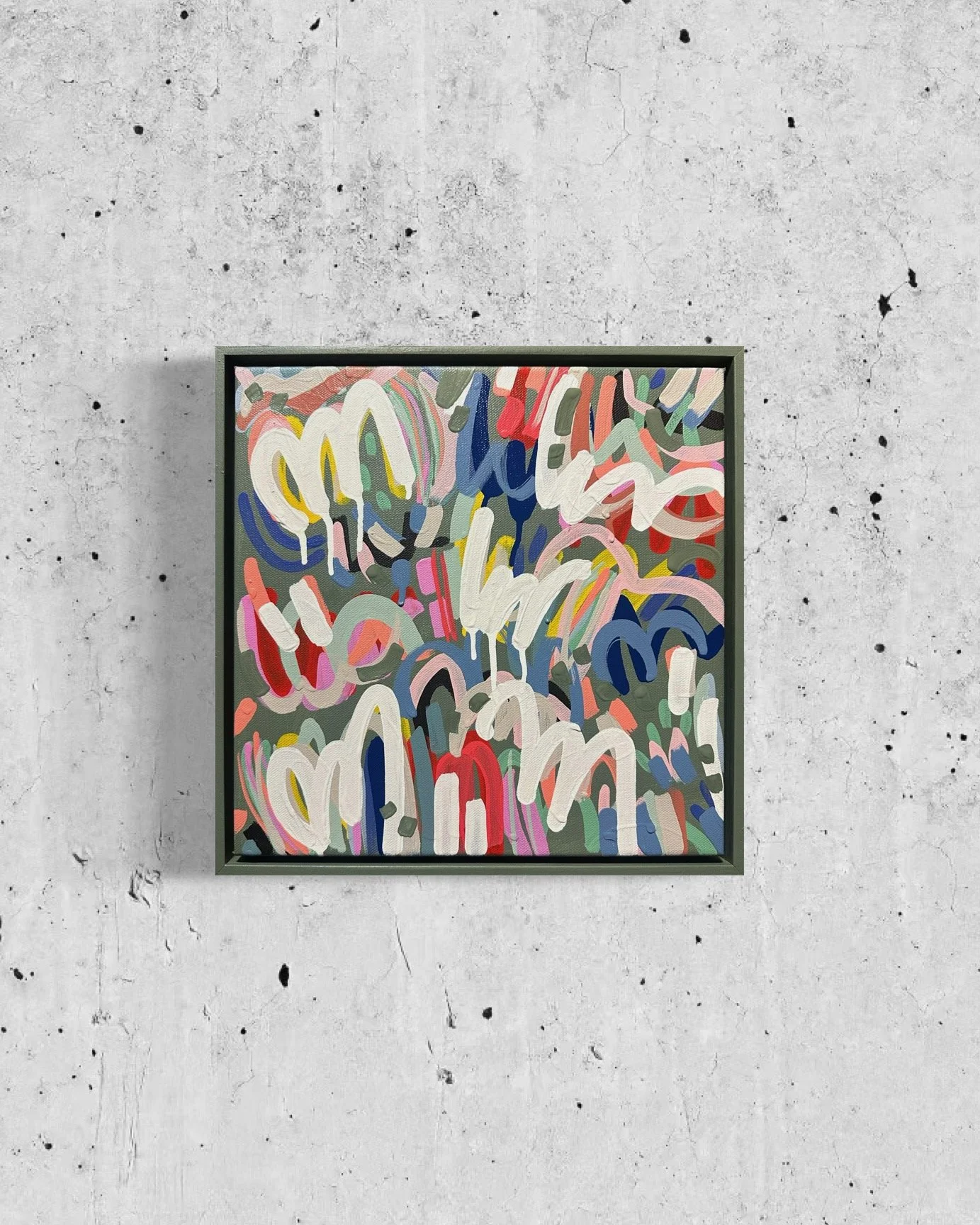 Abstract colorful painting with white, yellow, blue, red, pink, and green brushstrokes on a gray background, framed and hung on a textured concrete wall.