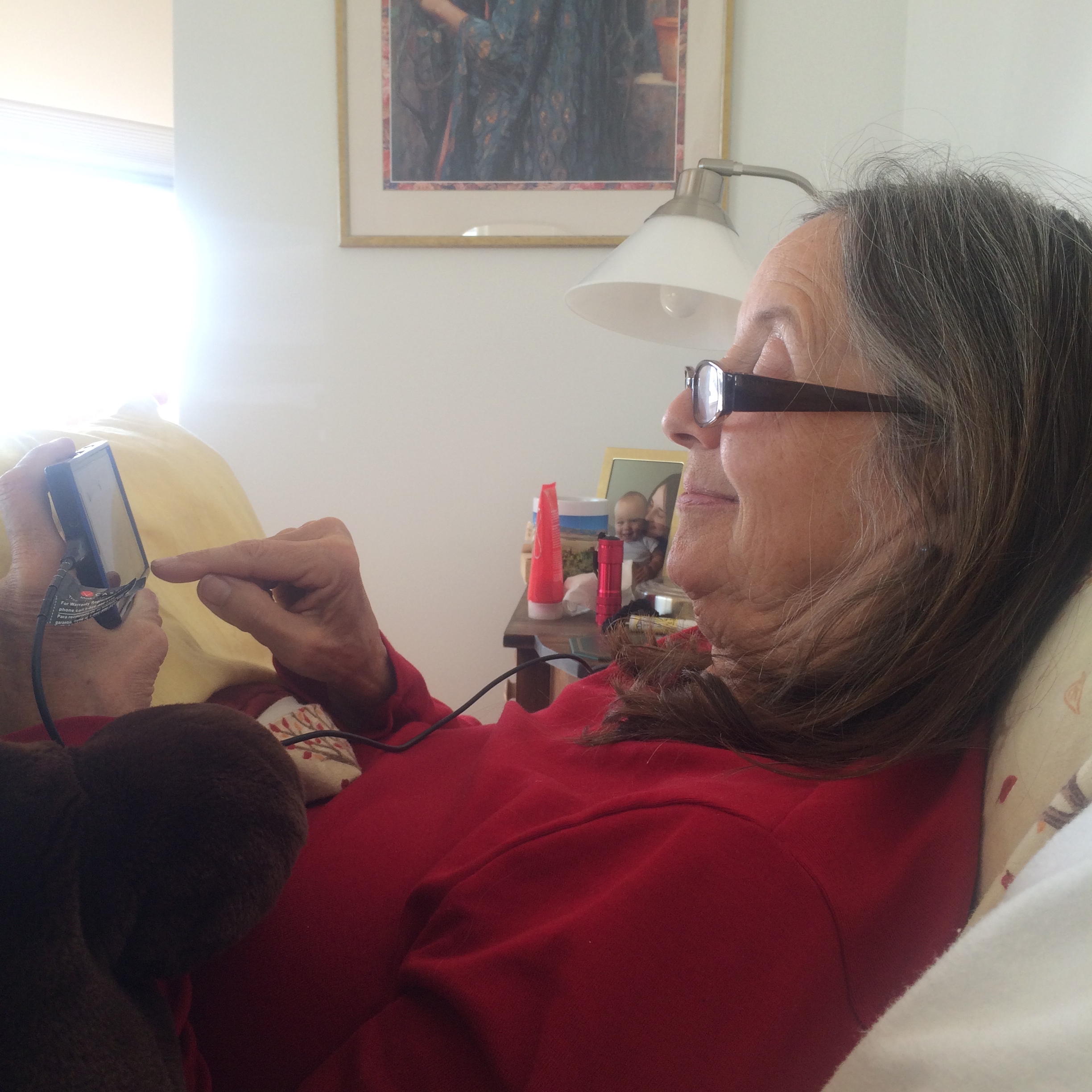 Sal in bed, drinking hot chocolate and watching videos of our grandson Drake playing with his bib.