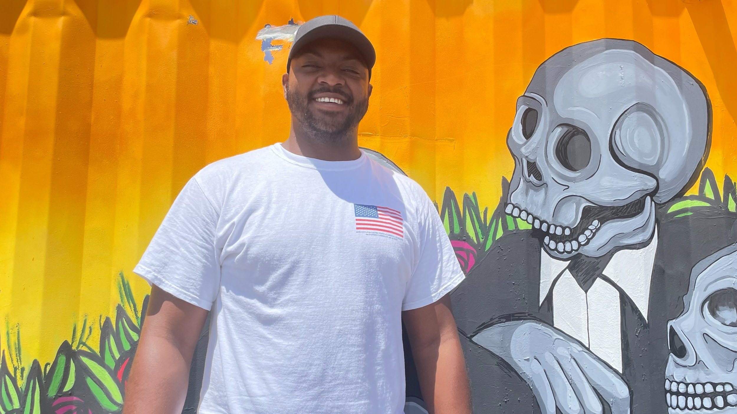 Johann Callendar, wearing an American flag T-shirt, stands in front of a mural.