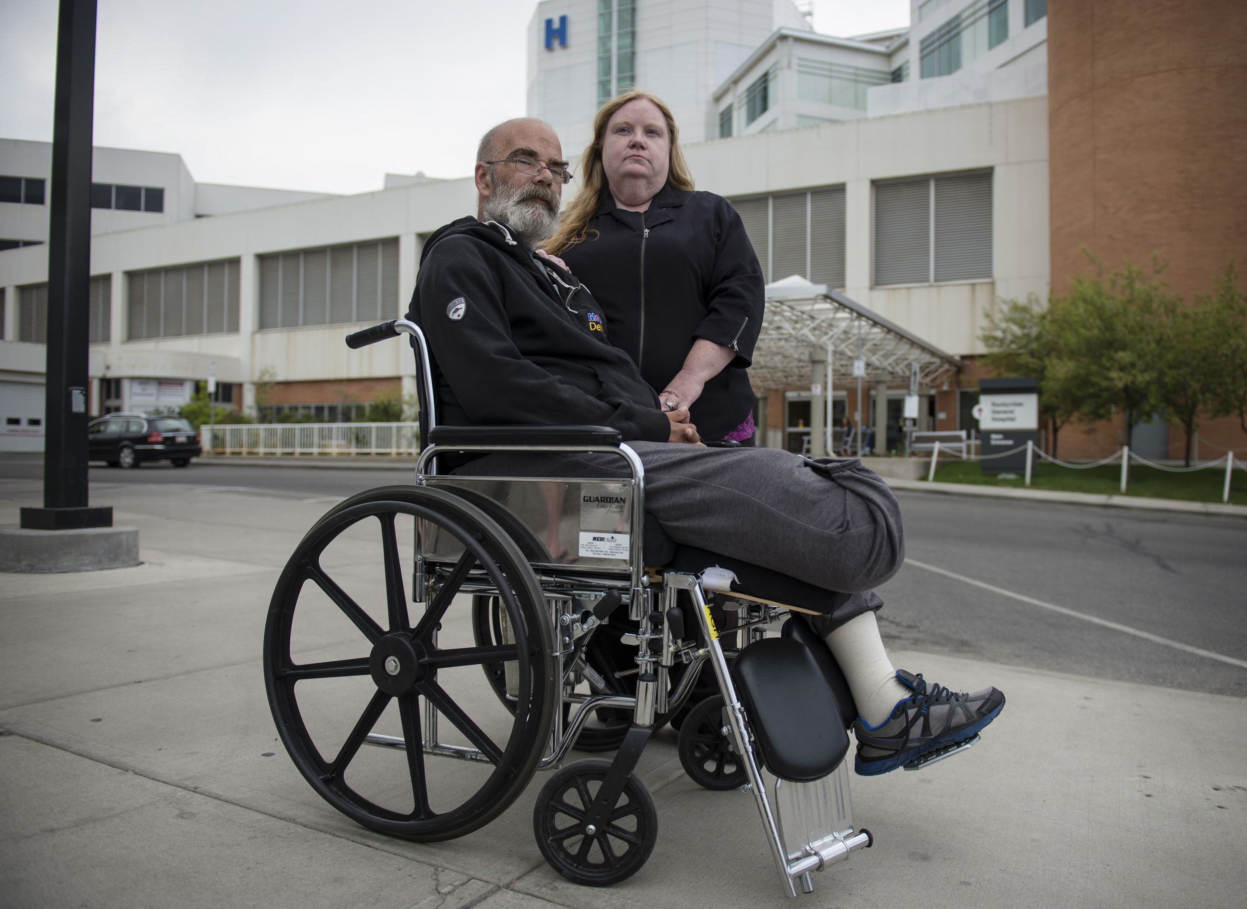 Ron and Pam Smith stand outside Calgary's Rockyview General Hospital on May 25, 2015. Since having his leg amputated a month earlier, Ron has been bound to a wheelchair, but due to "capacity issues," his room is too small for him to even get out of bed. "It's like a prison without the chain link fence," he said.