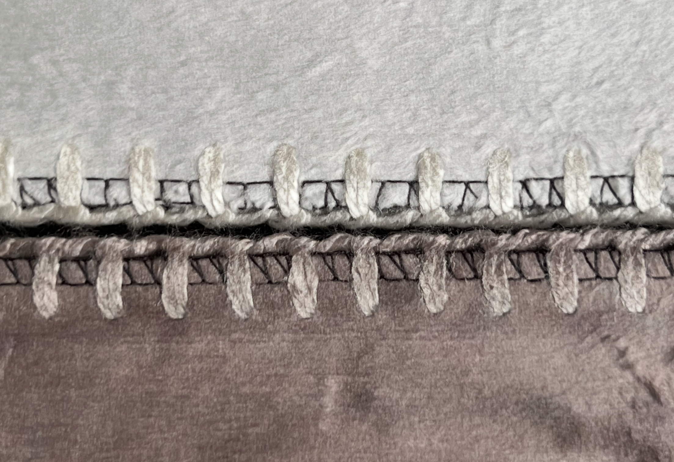 Extreme close-up of two CanvasDiscount photo blanket edges showing overlock stitching in two different tones — cream white on the lighter side and dusty rose on the darker printed side — demonstrating color-matched finishing