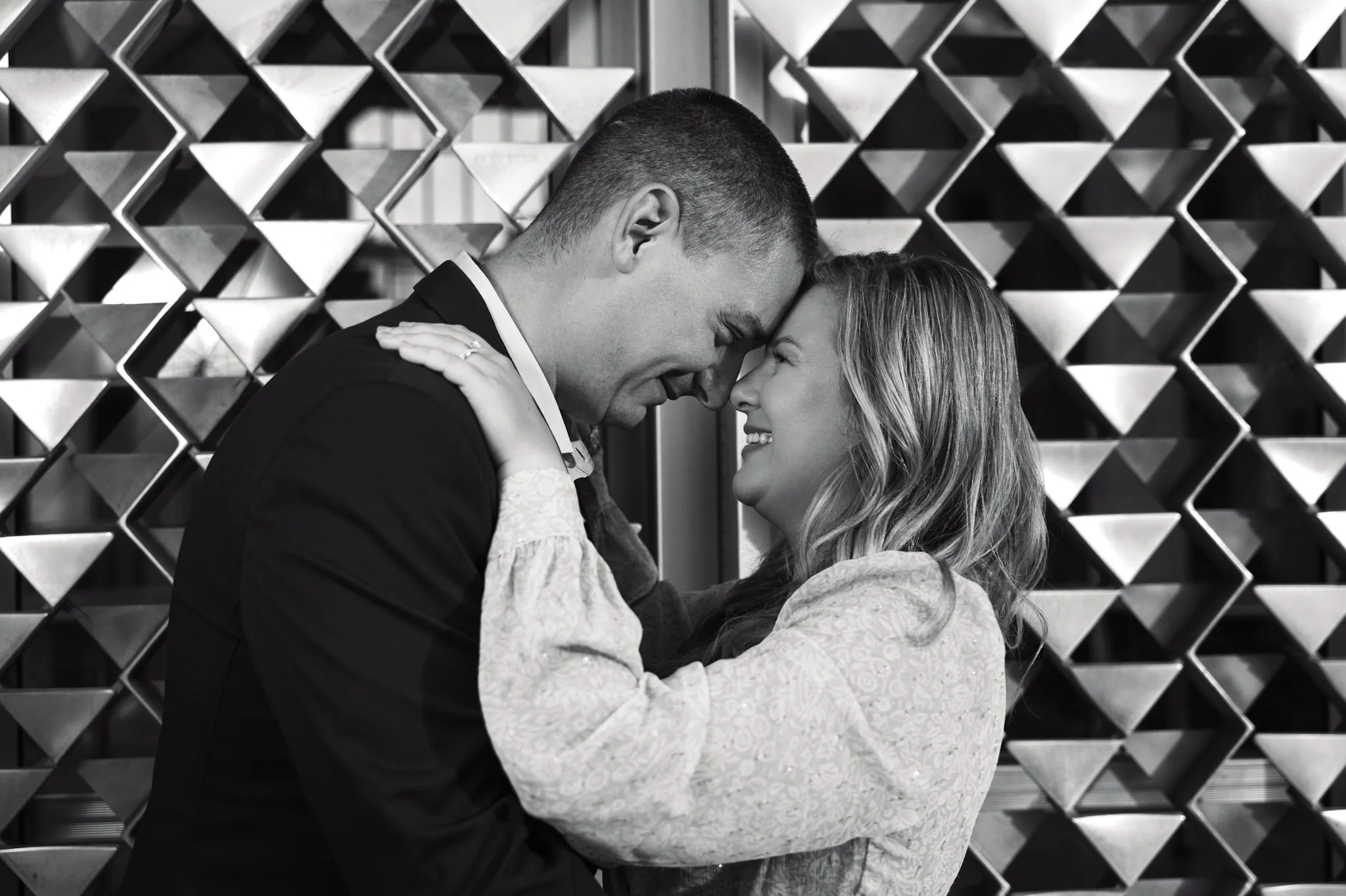 Caitlyn and Chad posing for their engagement photoshoot on Wayne State's campus in Detroit, showcasing a modern, urban setting with contemporary facades in the background.
