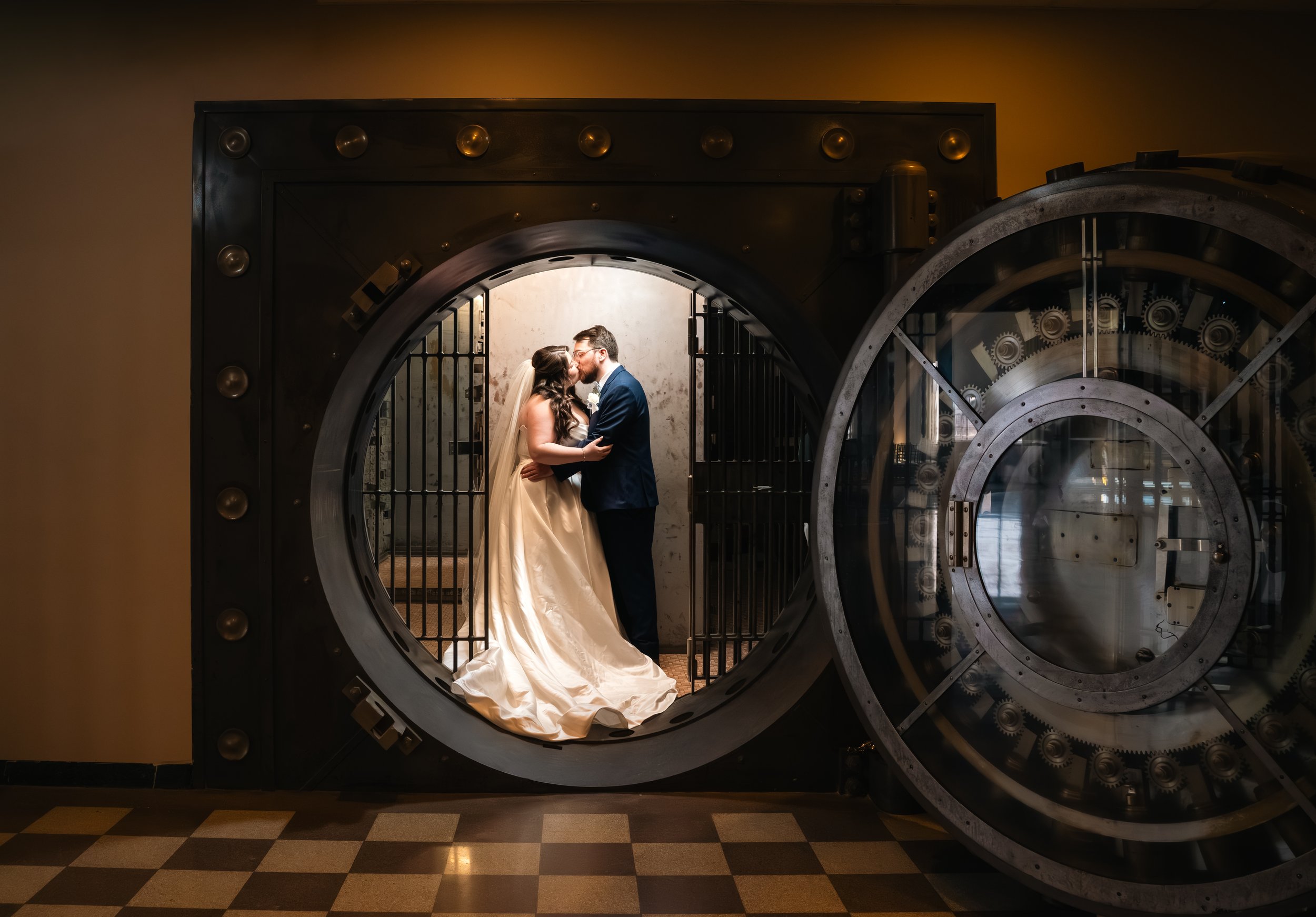 A bride and groom sharing a kiss inside a large, open bank vault door.