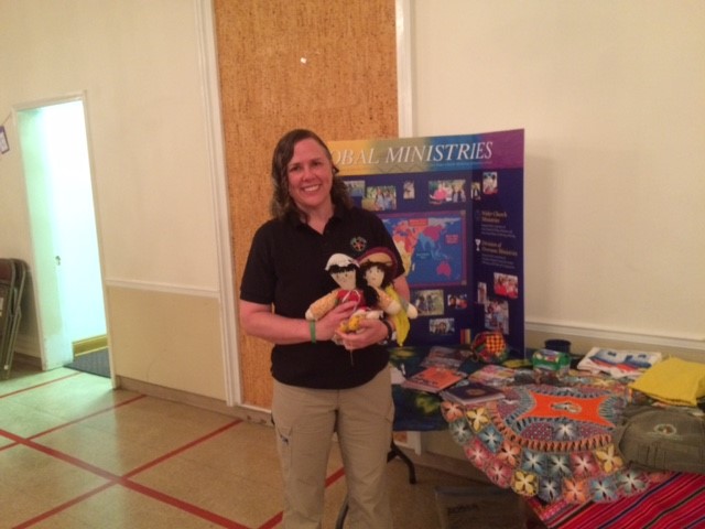 Elena showing various items on her display table. The dolls were made to help children who had experienced the trauma of the earthquake. The photo was taken at the Country Club Congregational United Church of Christ in Kansas City.