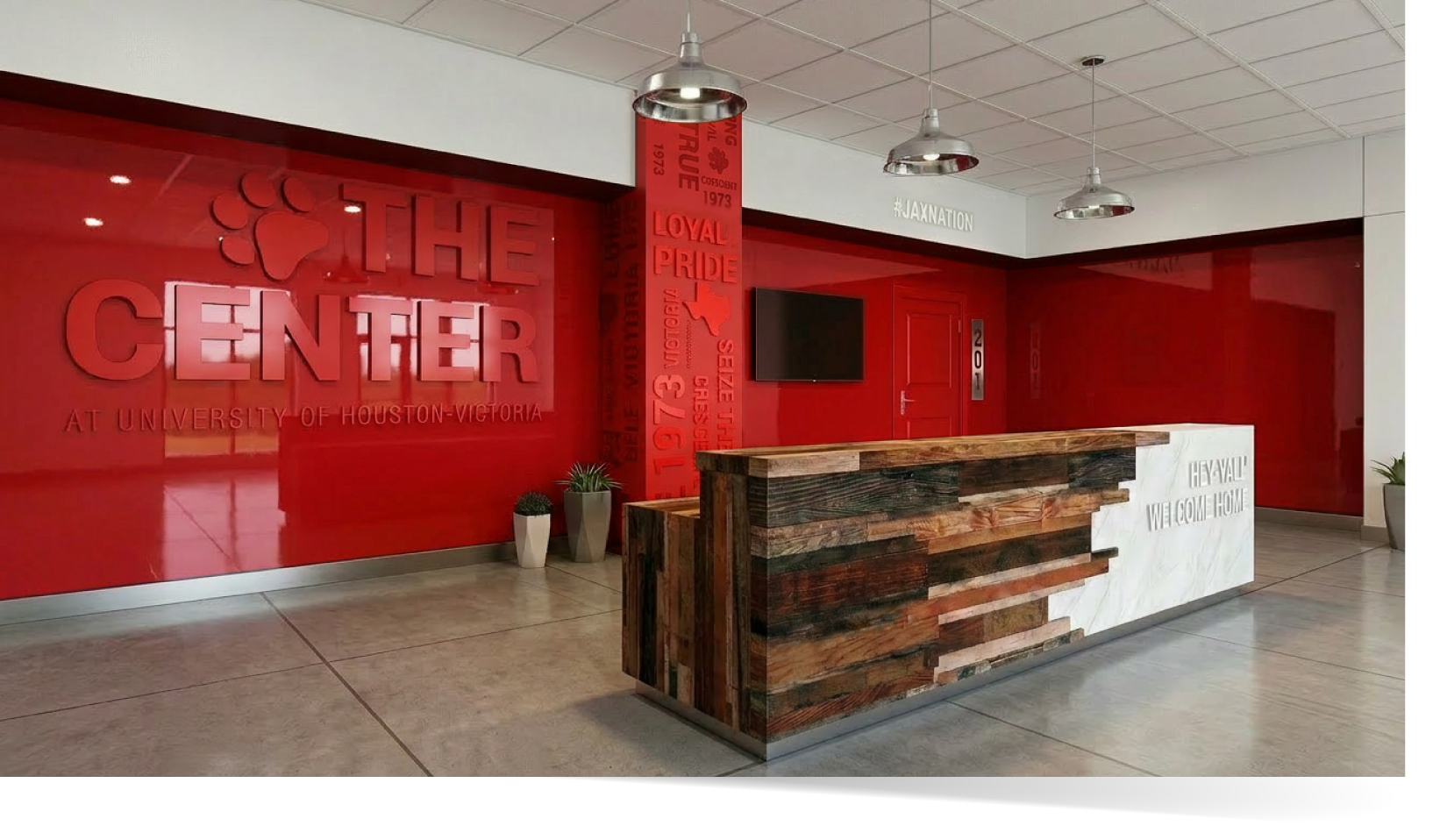 Final design of interior of The Center at UHV by Larzell Cowan of Fresh Fox Design Studio – red branded wall with 'THE CENTER' signage, custom wood and marble reception desk, and welcoming Texas hospitality elements.