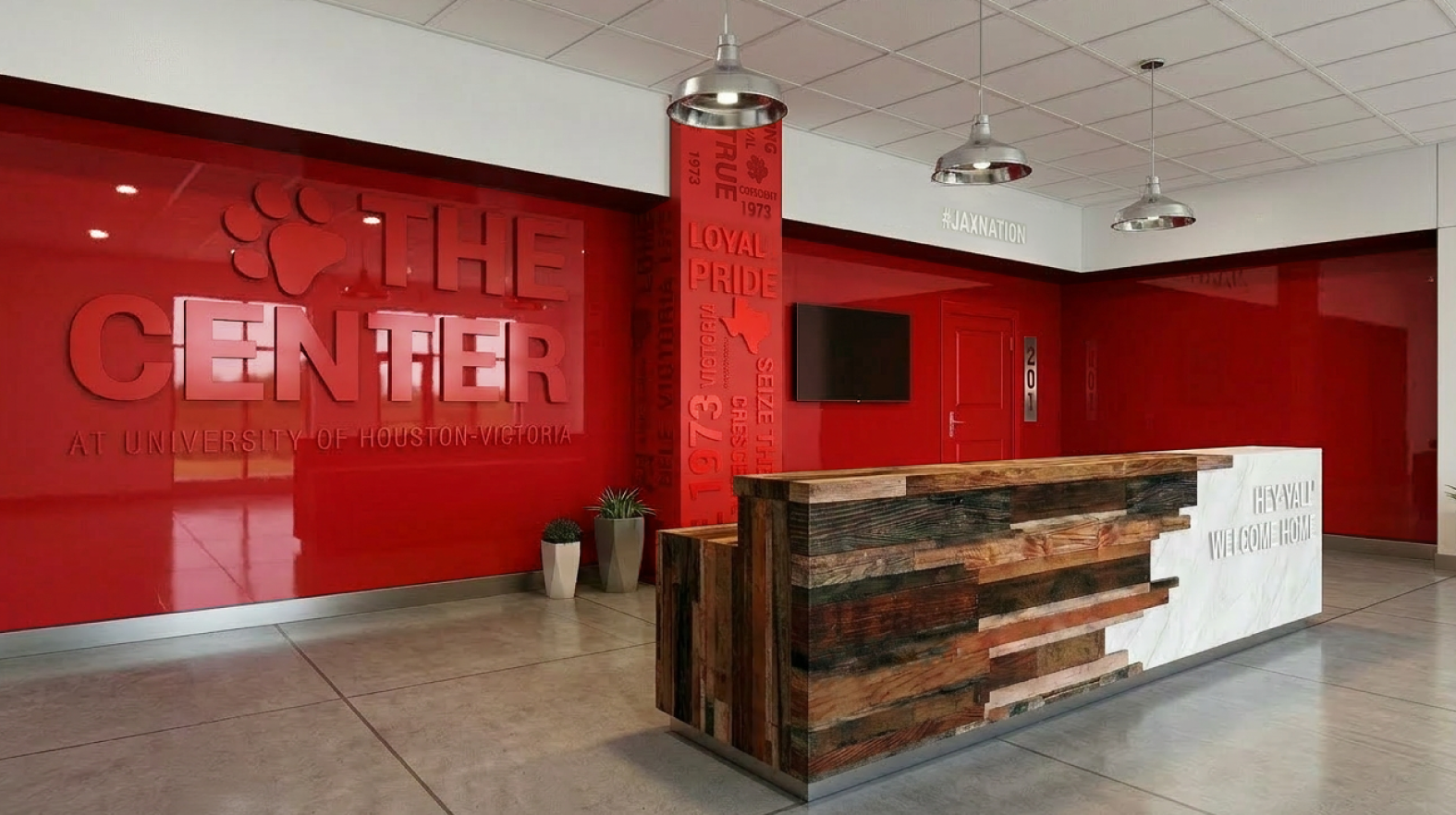 Final design of interior of The Center at UHV by Larzell Cowan of Fresh Fox Design Studio – red branded wall with 'THE CENTER' signage, custom wood and marble reception desk, and welcoming Texas hospitality elements.