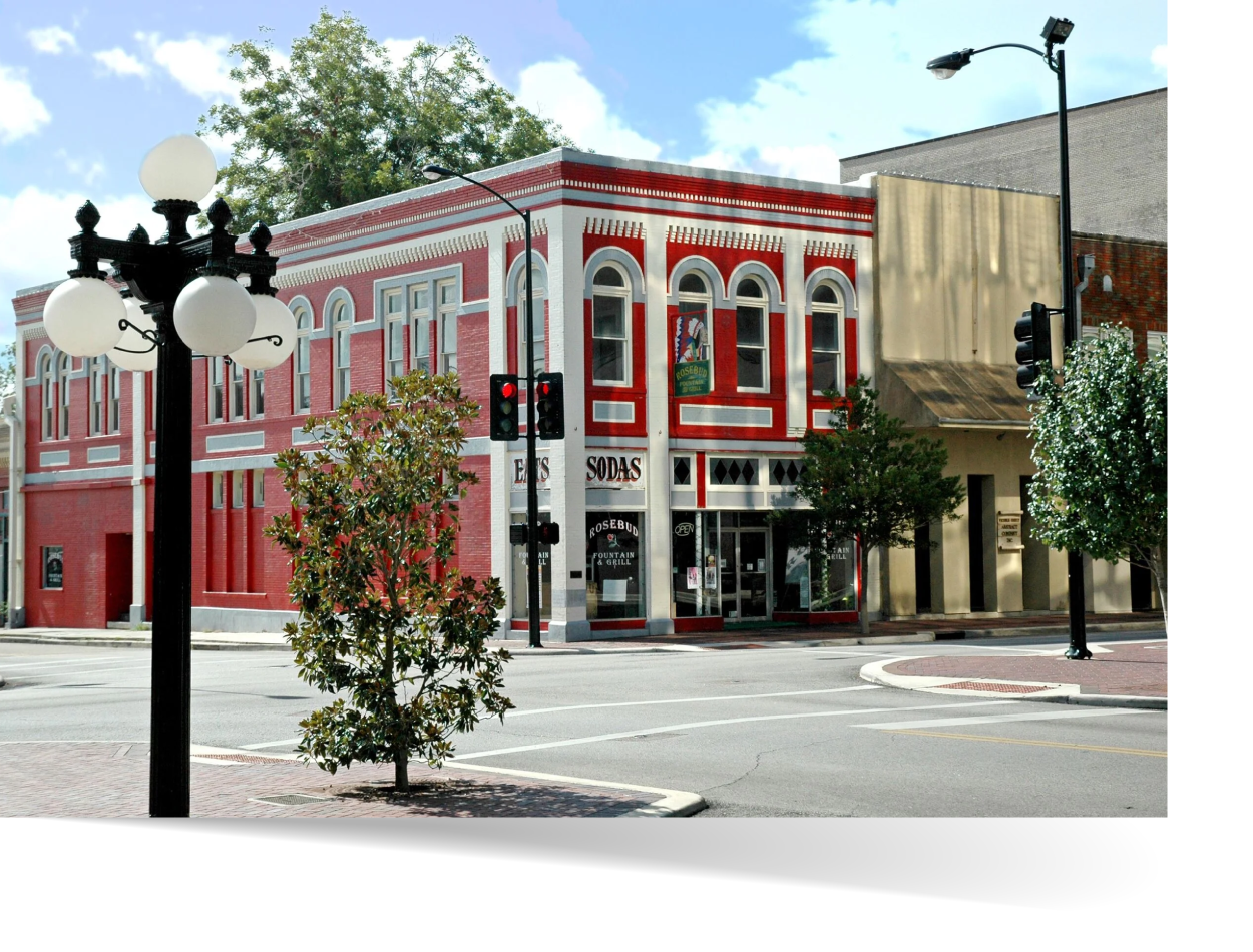 Historic red brick buildings and storefronts along a sunny street corner in downtown Victoria, Texas, with a vintage lamppost in the foreground.