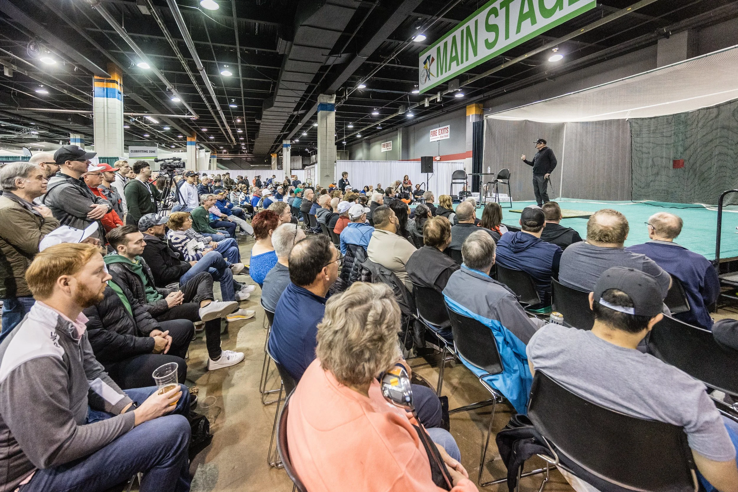 The Main Stage at the Chicago Golf Show with many people sitting and standing, facing the stage where a speaker Hank Haney is presenting.