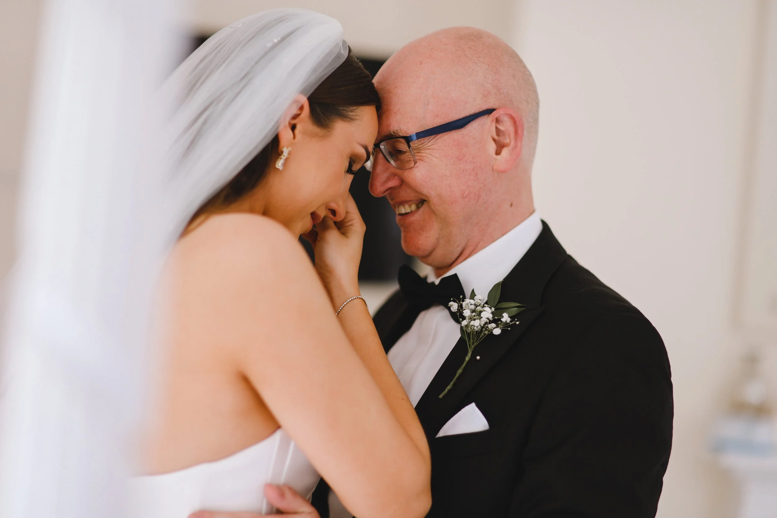 Bride embracing an older man in a tuxedo, both smiling, with a bridal bouquet on his lapel.
