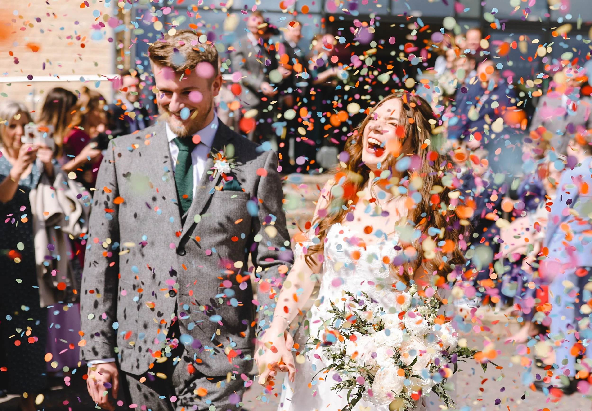 Bride and groom surrounded by confetti outdoors at wedding.