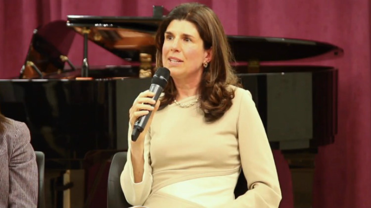 Nancy M. Williams speaking into a microphone to tell her personal hearing loss story, with a piano in the background