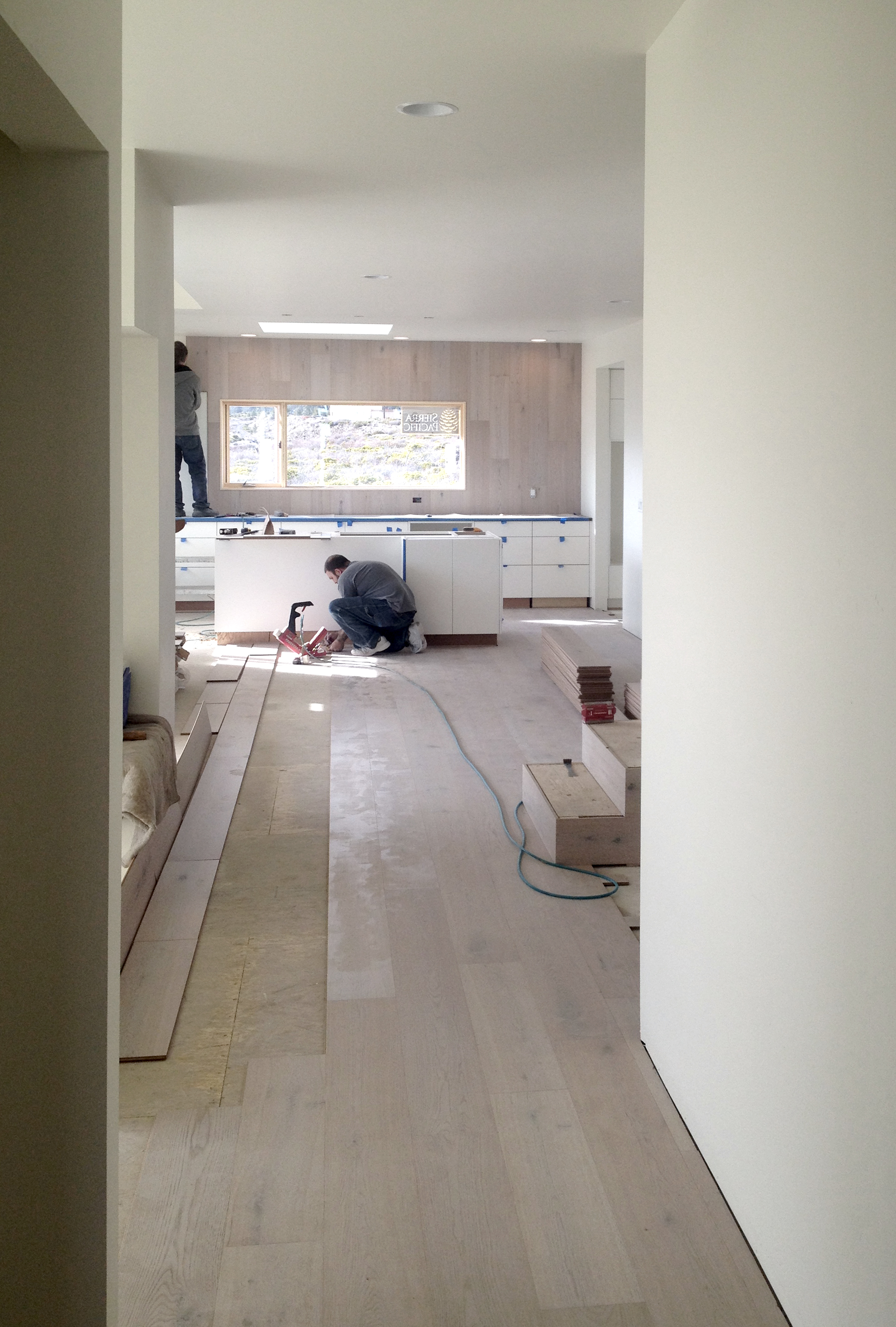 Lot 7 - Wood flooring being installed, wrapping up the wall beyond the kitchen cabinetry