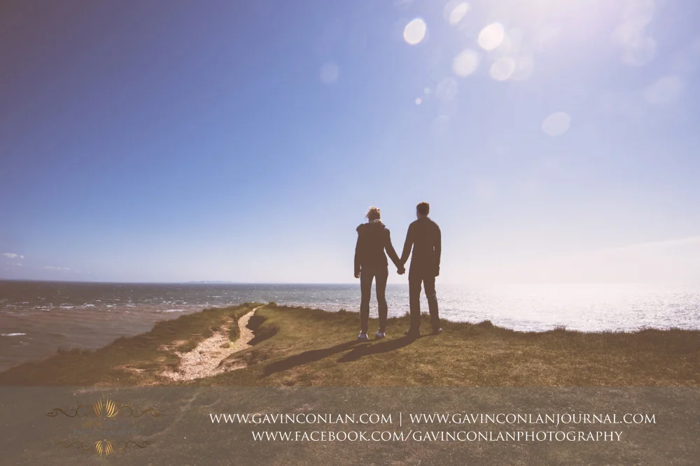 creative portrait of the couple holding hands looking out over the Solent on the edge of the chalk ridge at Old Harry Rocks . Victoria and James Engagement Session in Bournemouth, Dorset by gavin conlan photography Ltd