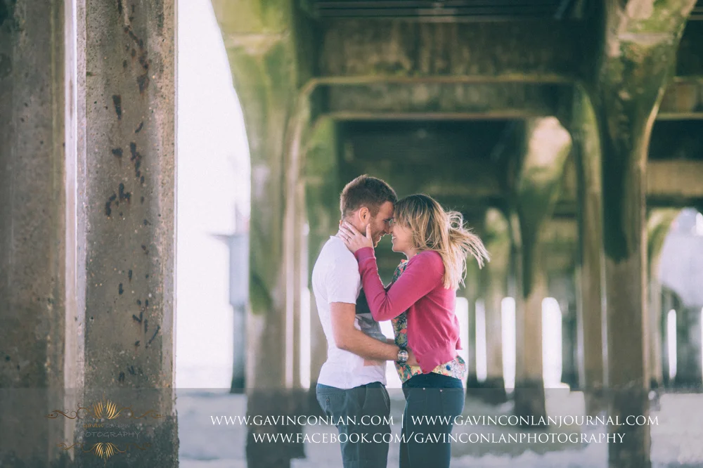 creative portrait of Victoria holding James' face just before she leans in to kiss him underneath Boscombe Pier . Engagement Session in Bournemouth, Dorset by gavin conlan photography Ltd