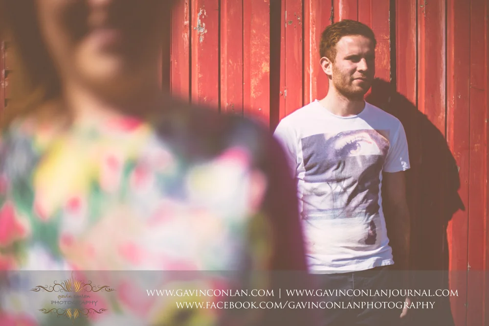 creative portrait of James in front of a red beach hut at Boscombe Pier . Victoria and James Engagement Session in Bournemouth, Dorset by gavin conlan photography Ltd