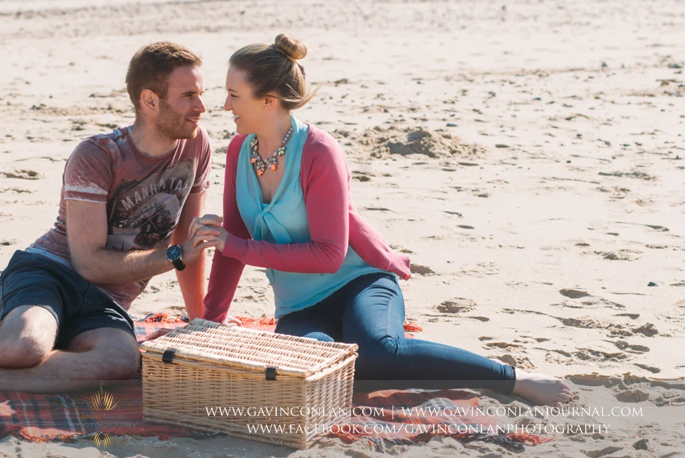 portrait of Victoria and James holding hands sitting on the beach near Boscombe Pier . Engagement Session in Bournemouth, Dorset by gavin conlan photography Ltd